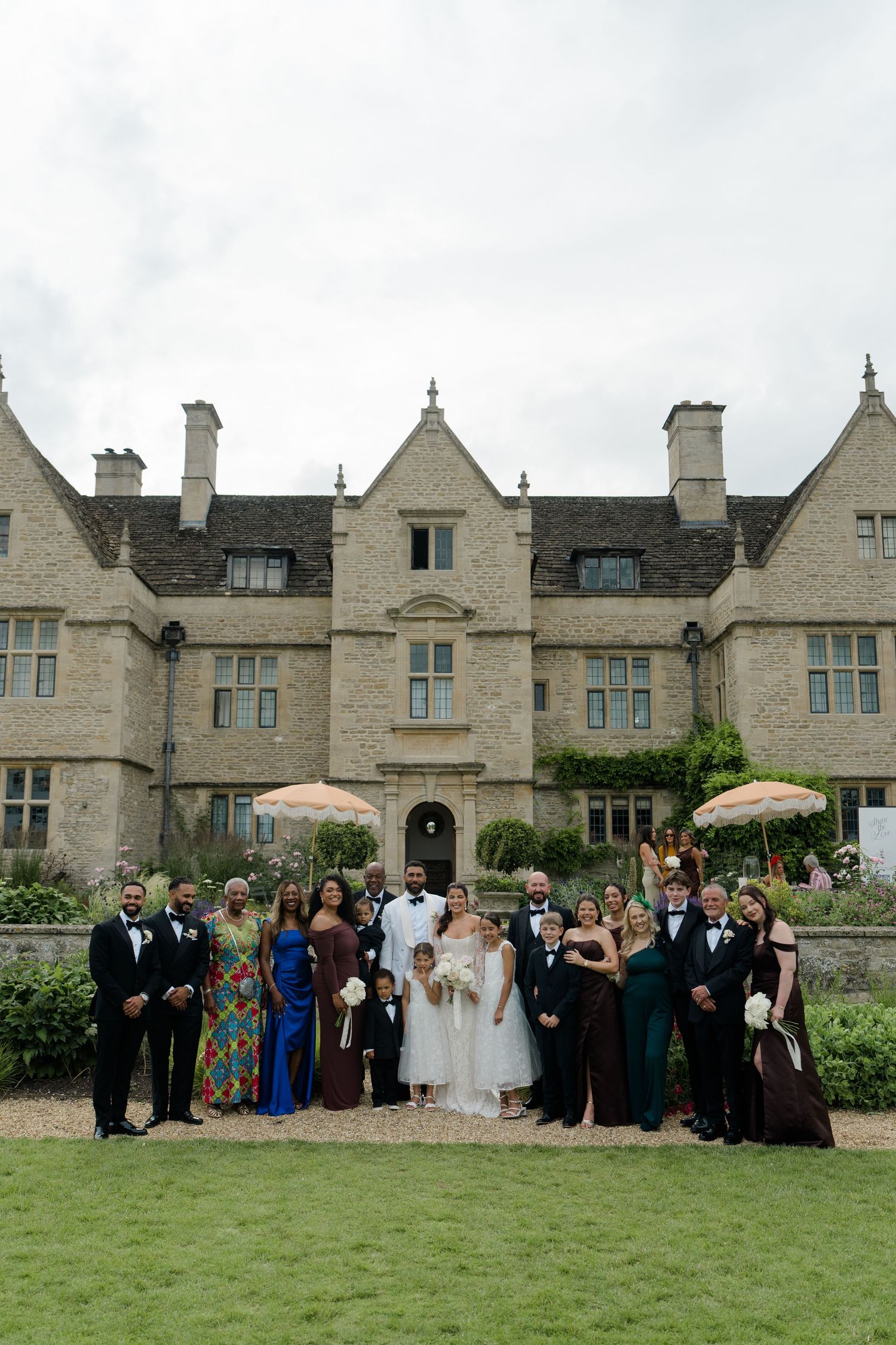 Wedding party poses in front of a grand stone manor house on a cloudy day.