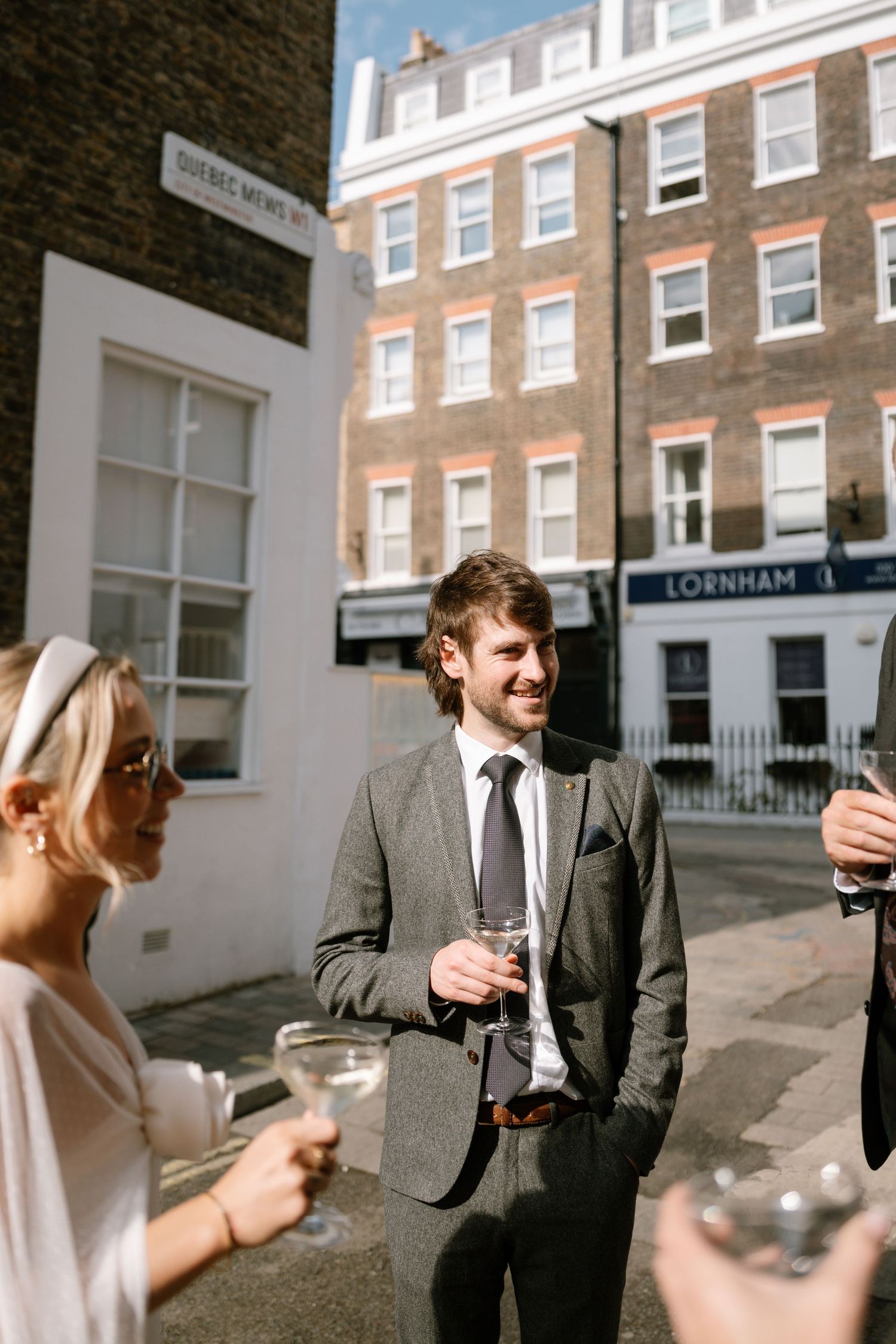 A couple shares drinks and laughter outside a brick building on a sunny day.