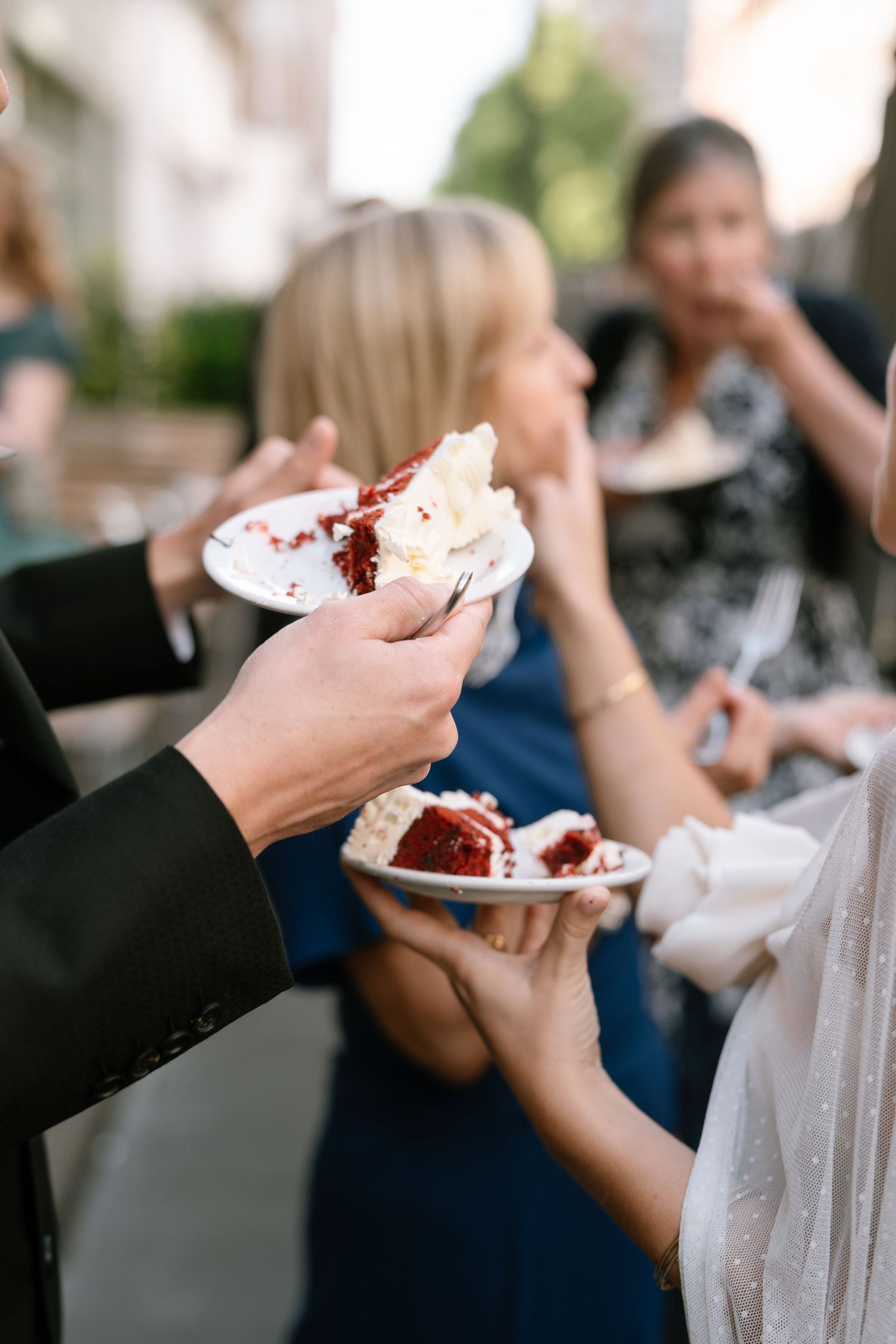 Wedding guests holding plates of red velvet cake at an outdoor reception.