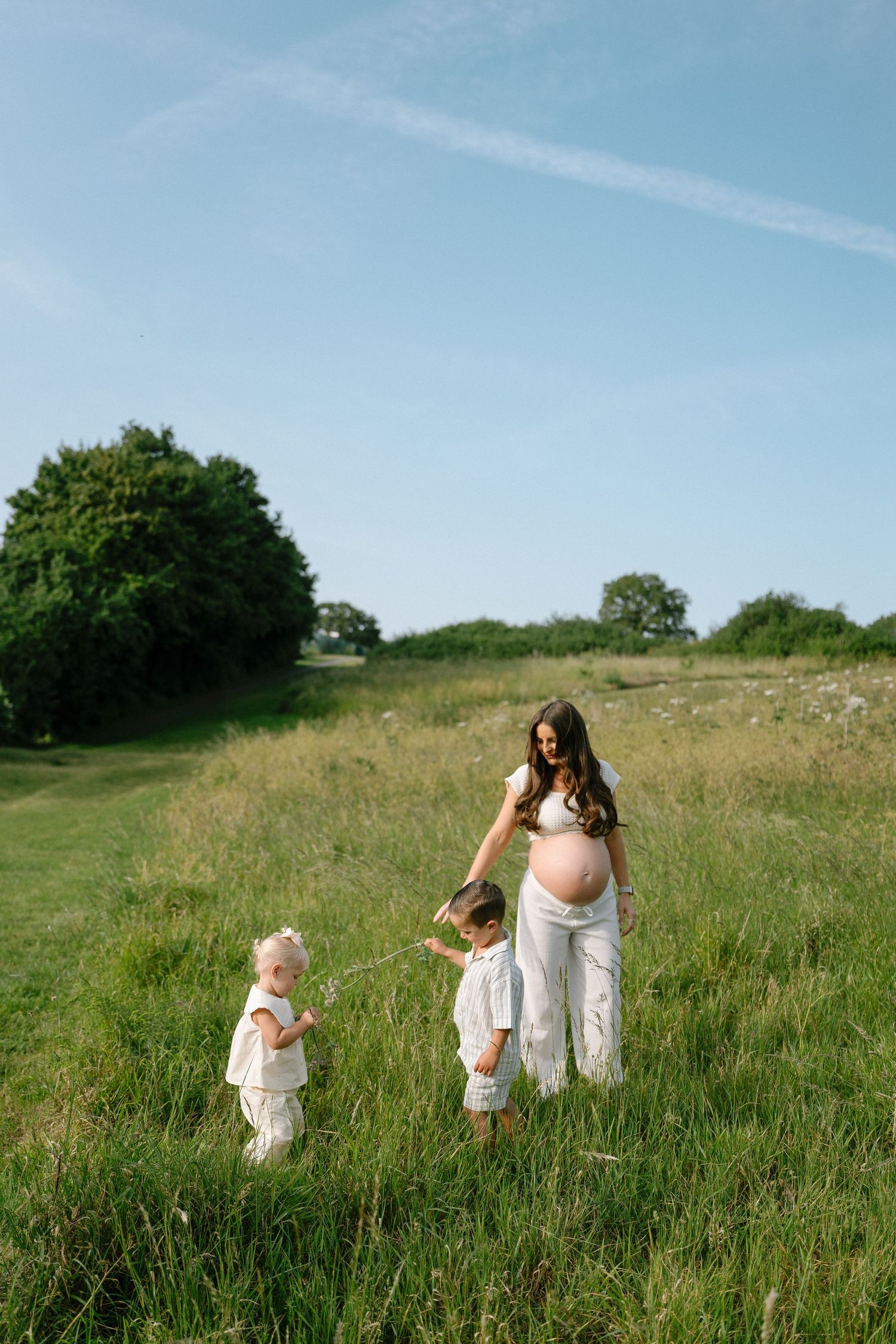 Family walking together through a sunlit meadow wearing white clothing.