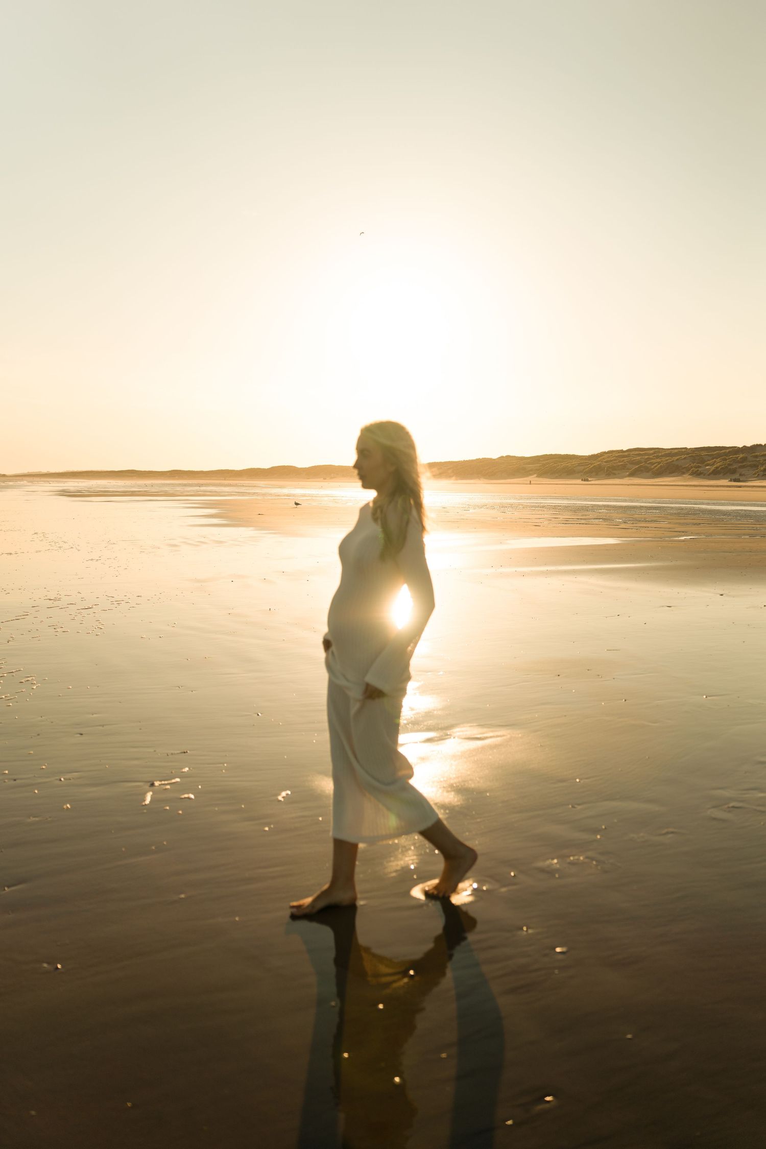 Silhouette of a person walking on a beach at sunset with golden light reflecting on wet sand.