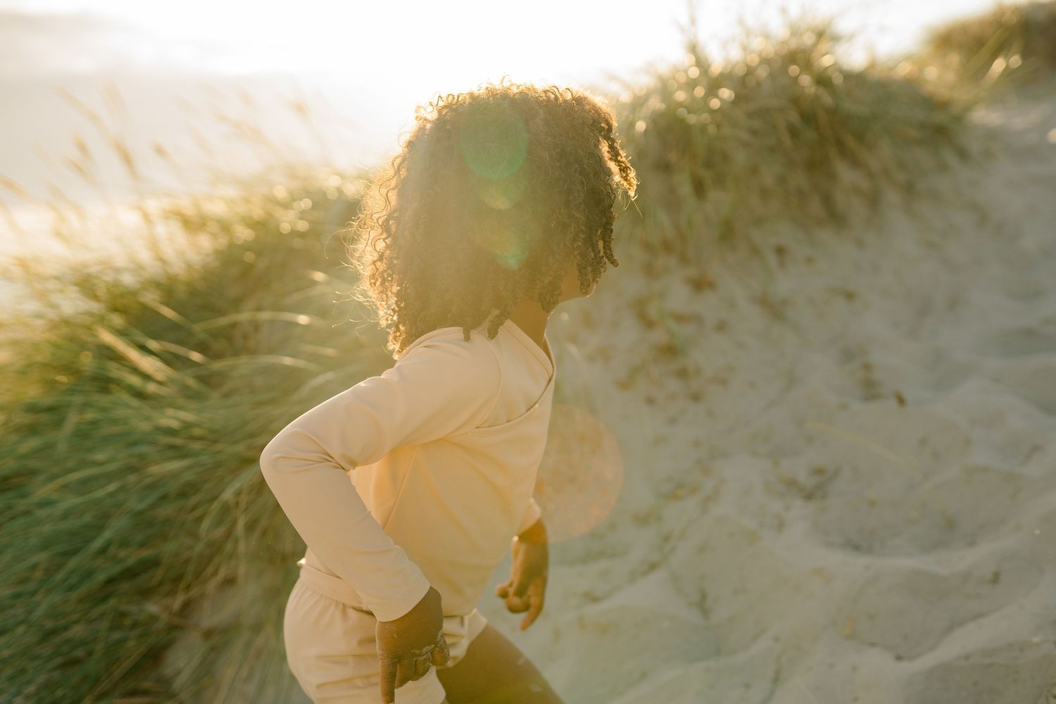 Person exploring coastal dunes with beach grass at golden hour.