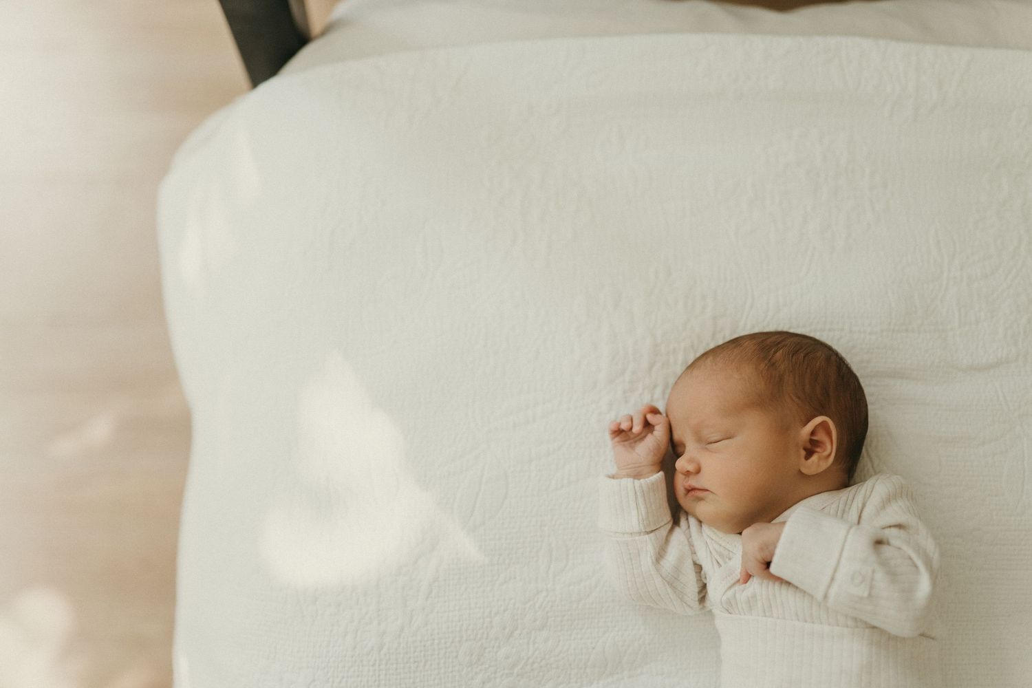 A newborn resting peacefully on white bedding in a sunlit room.