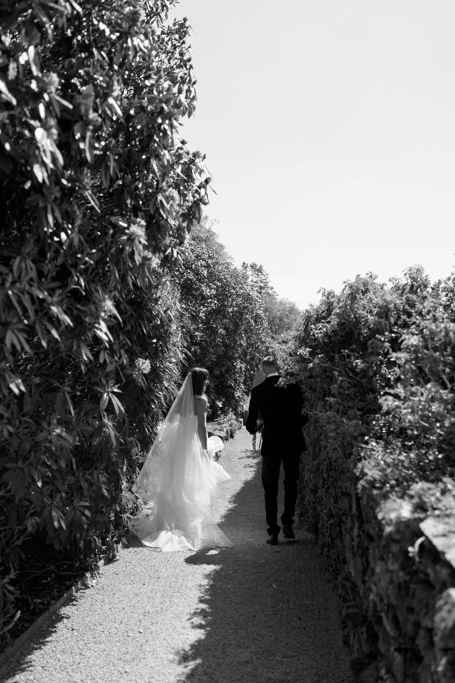 Black and white photo of wedding party walking down a gravel garden path.