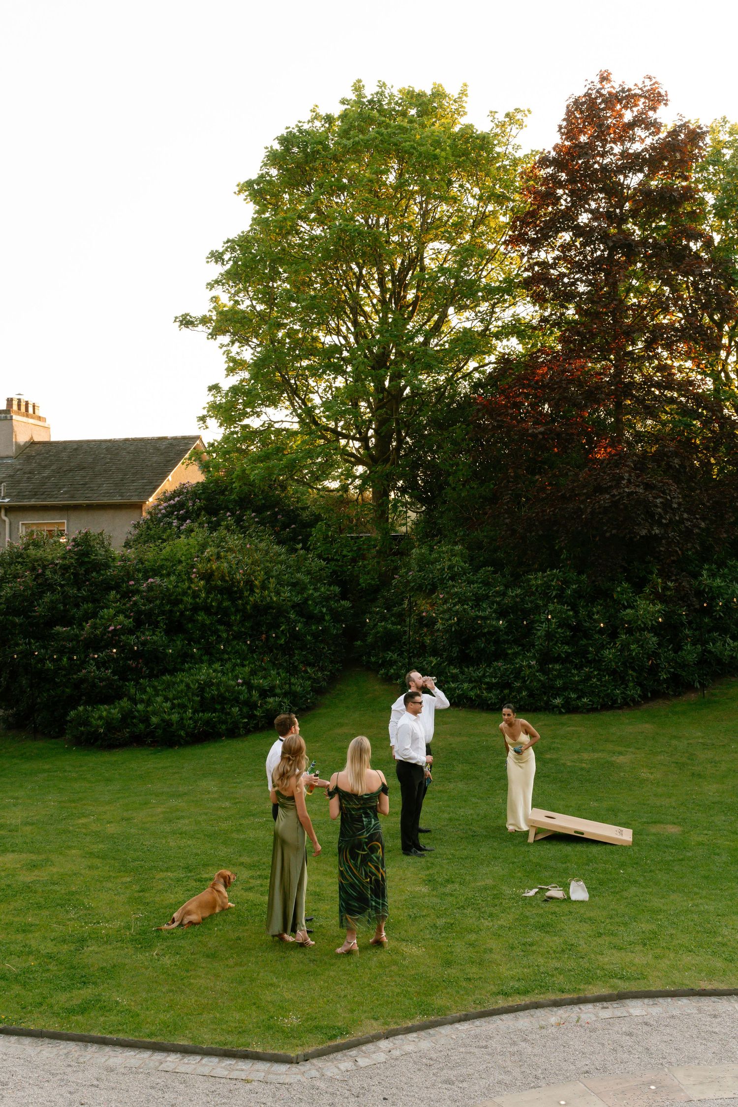 Wedding guests play lawn games including cornhole on a grassy area during an outdoor reception.