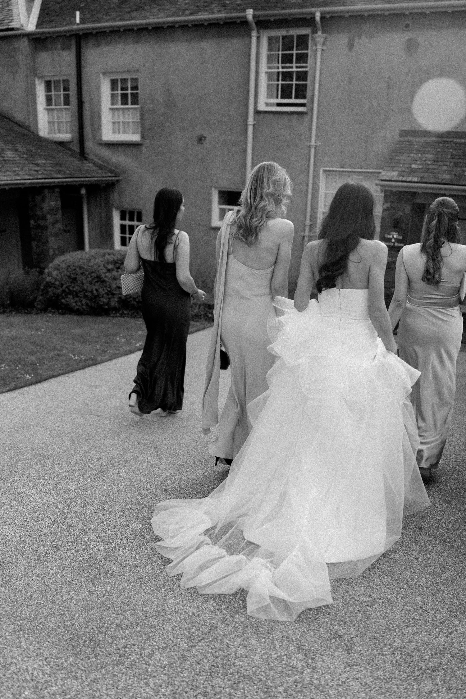 Group walking outdoors in formal wedding attire with flowing white dresses.