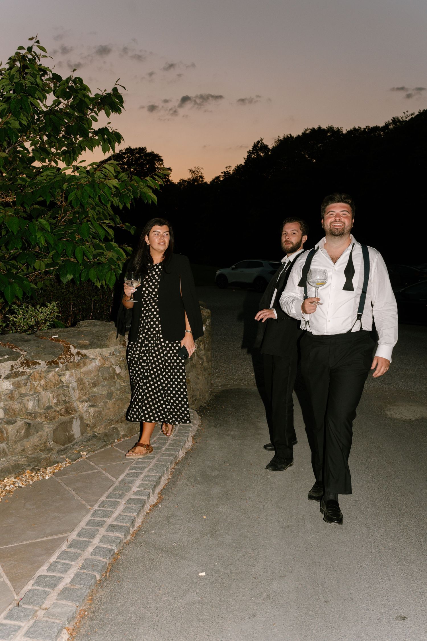 Group of wedding guests walking along a stone path at dusk.