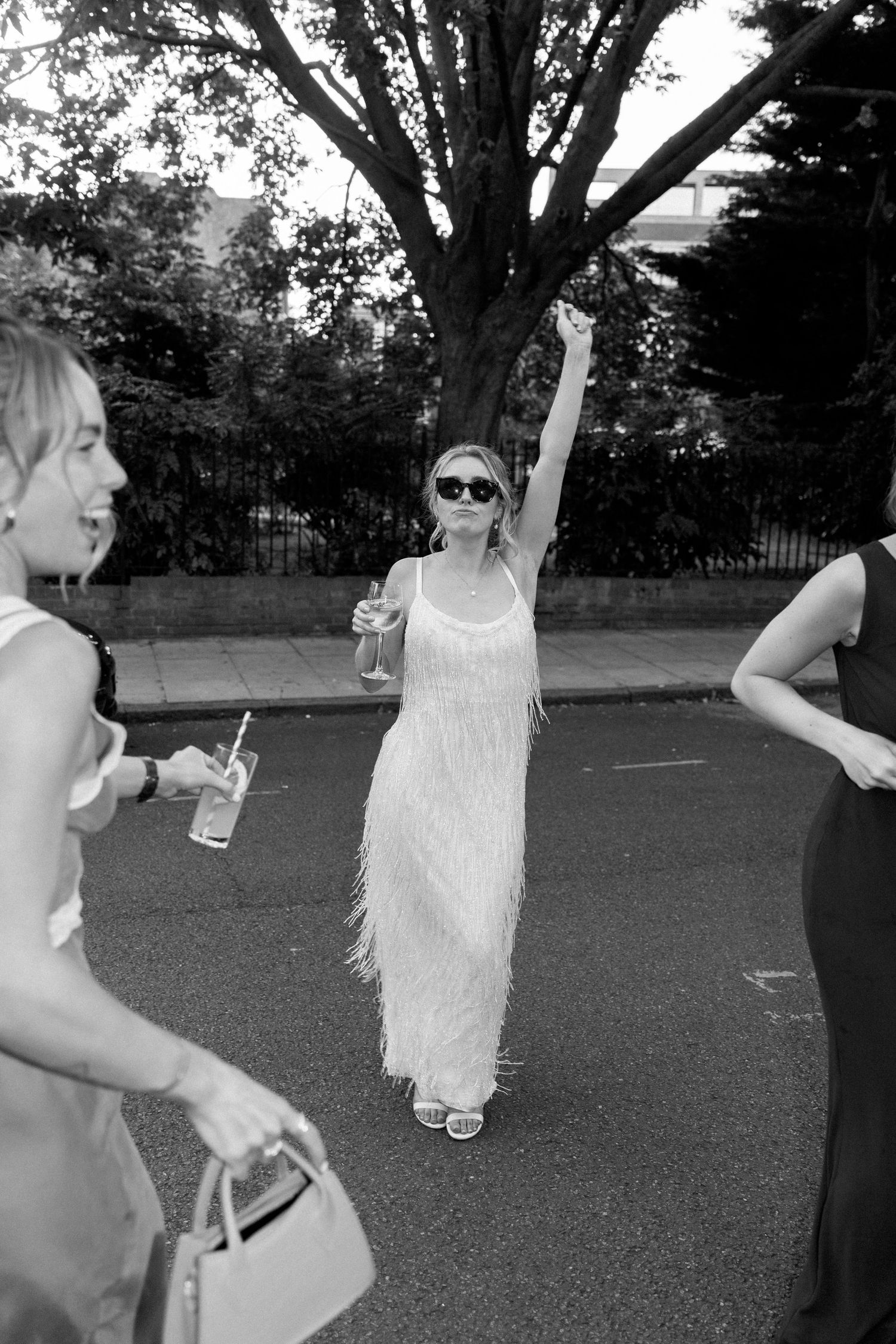 People celebrating outdoors with drinks, featuring a woman in white fringe dress.