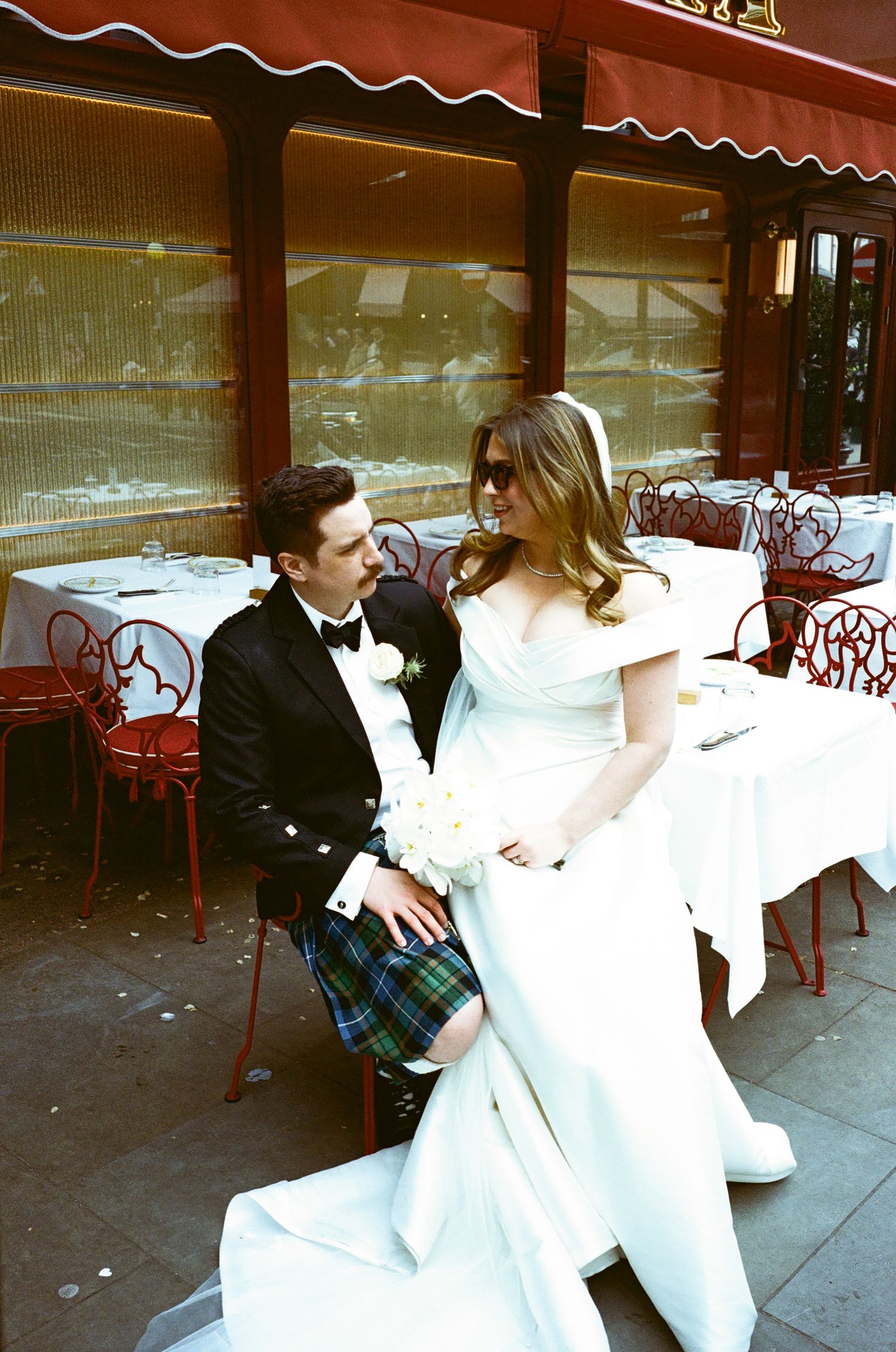 A sequence of four connected photos showing a couple in formal attire dancing and twirling outside a cafe with red awnings.