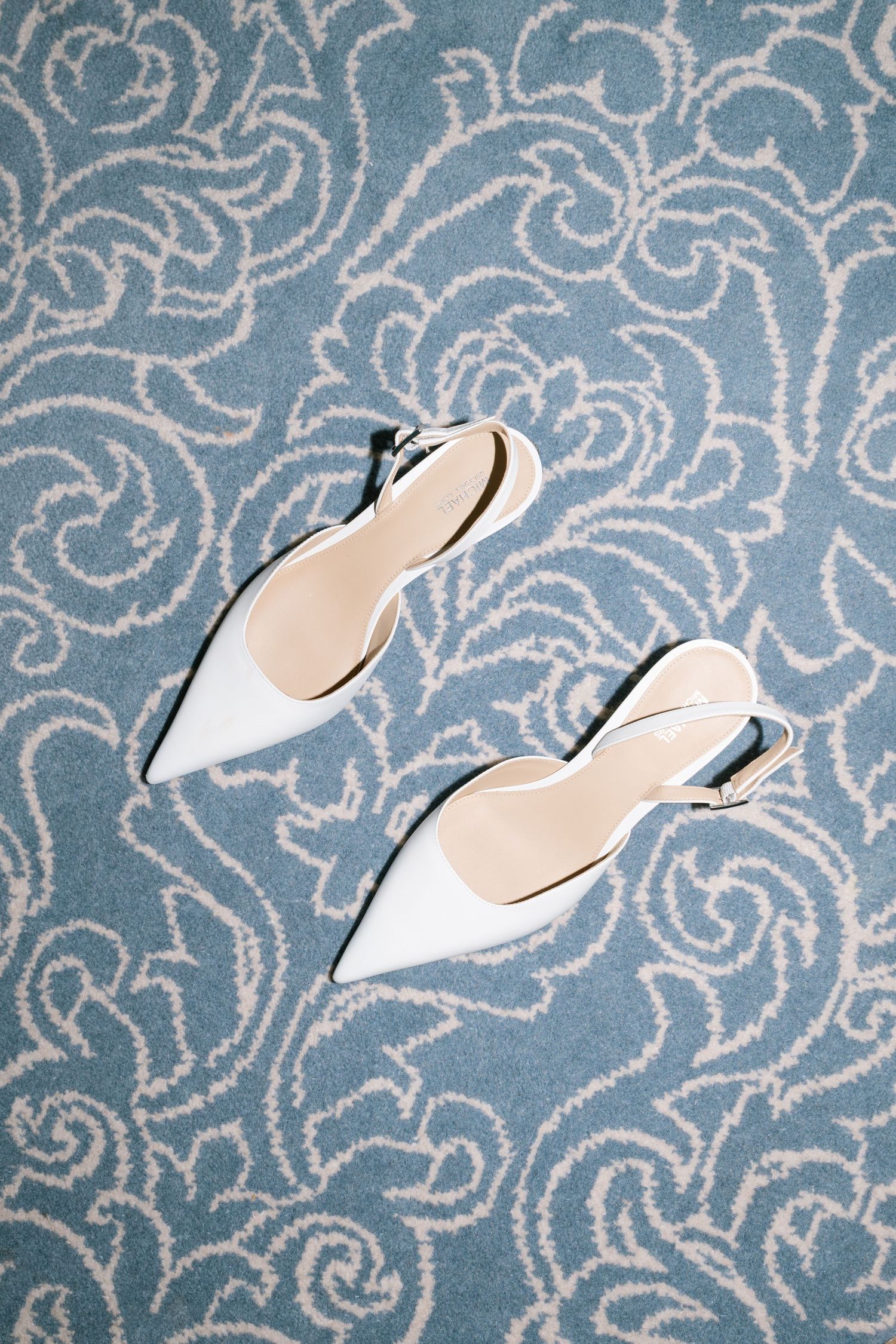 White pointed bridal shoes against a blue and white patterned background.