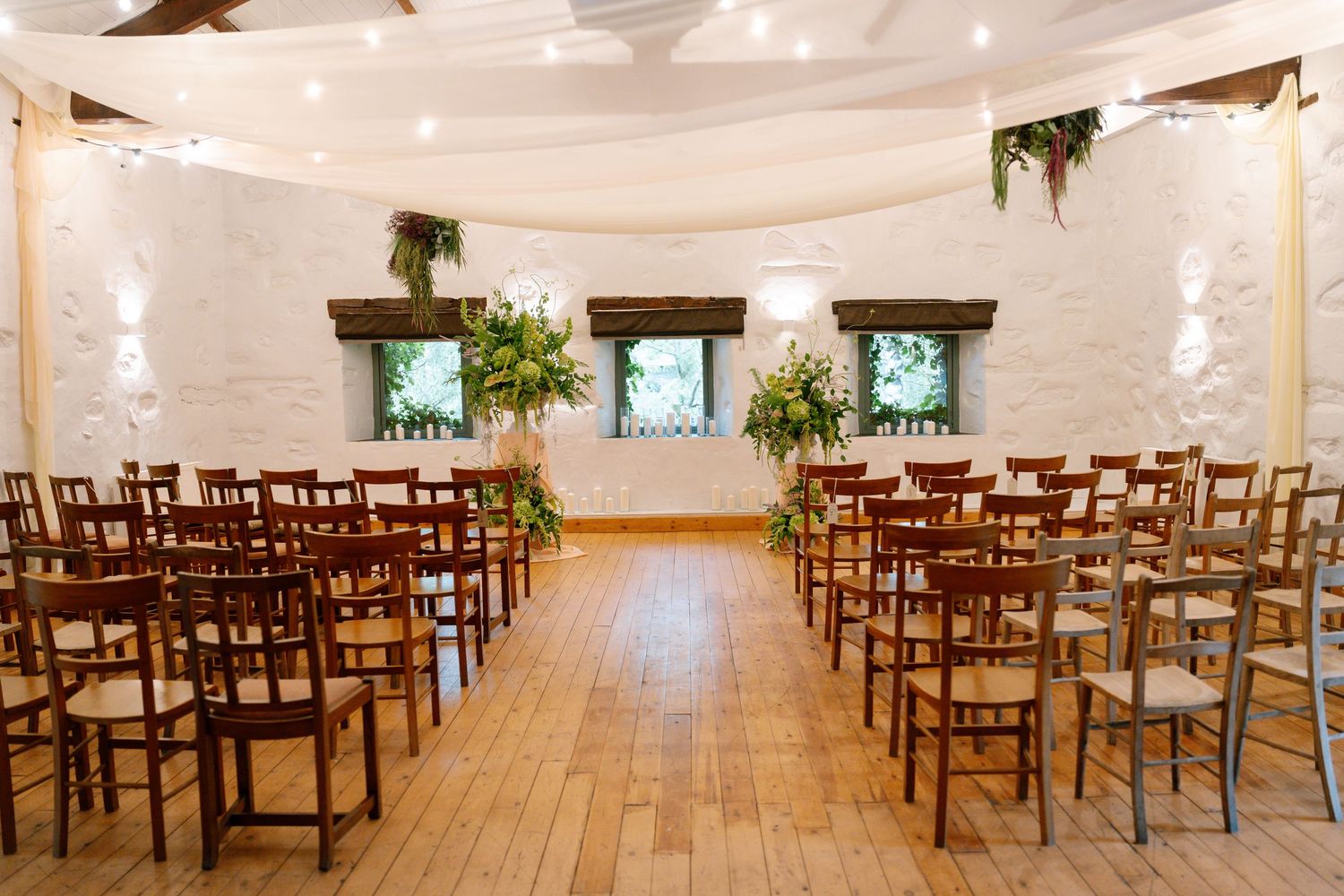 Elegant wedding venue interior with rows of wooden chairs and white fabric draping creating a romantic atmosphere.