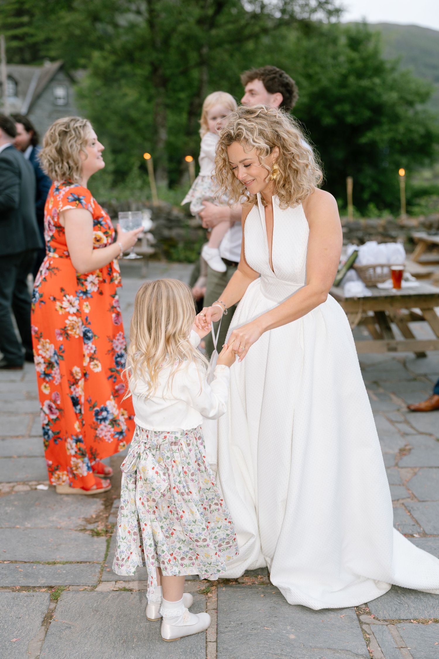 Wedding guests and children gather on a stone patio during an outdoor celebration.