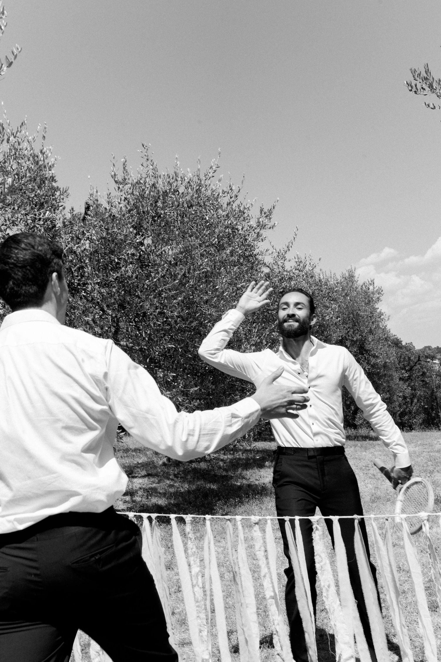 Black and white photo of people dancing joyfully on an outdoor patio surrounded by trees.