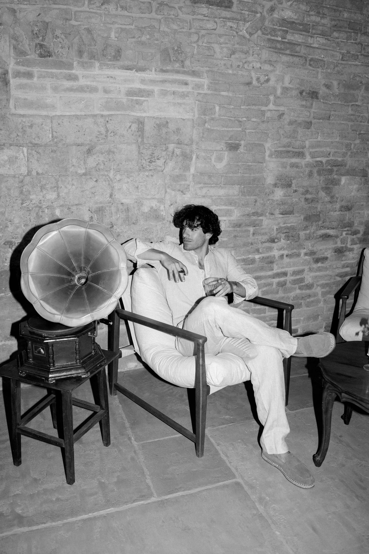 Black and white photograph showing a row of vintage phonograph horns displayed on wooden chairs against a brick wall.