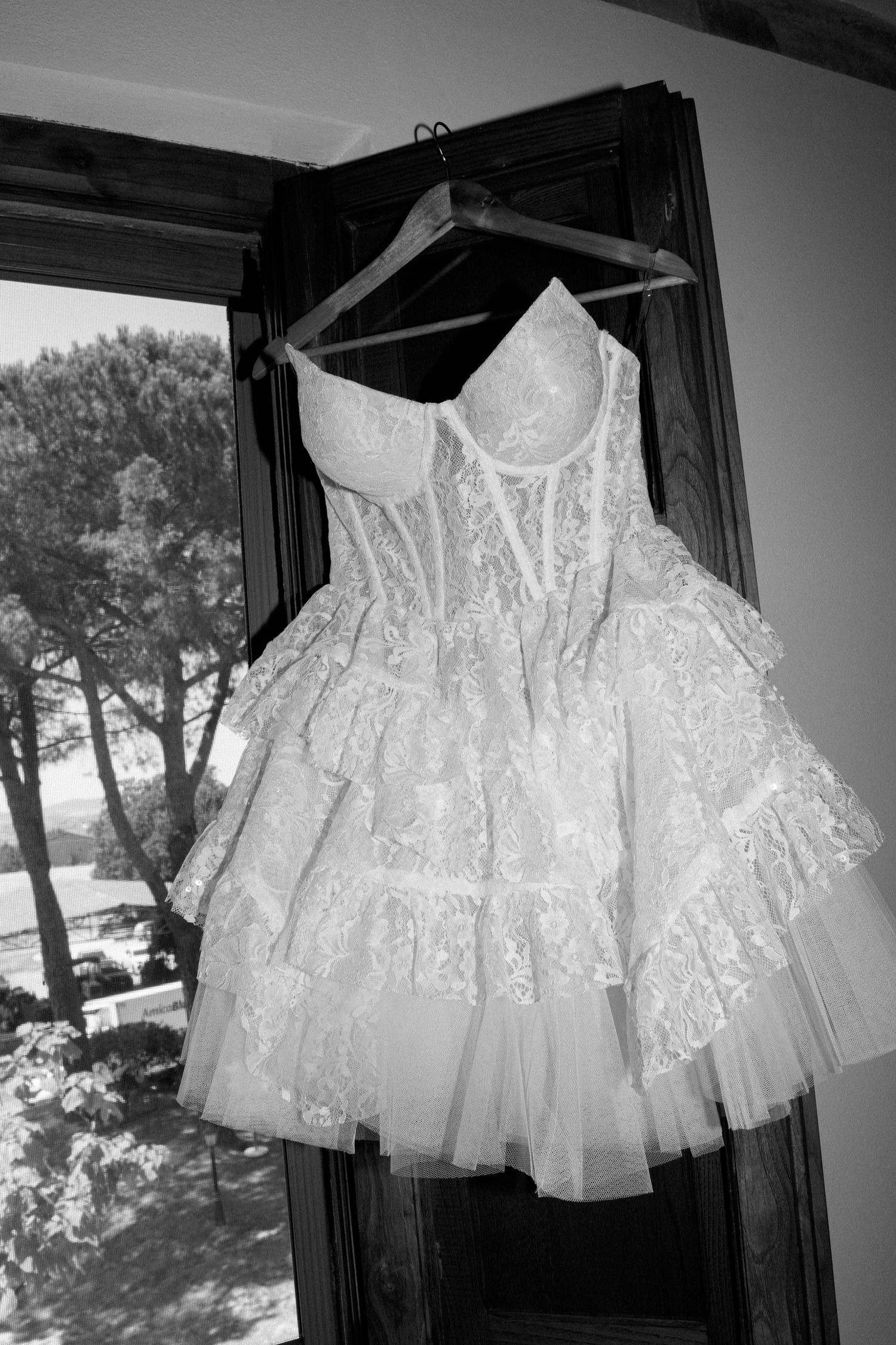 White lace christening gown with delicate details and ruffles displayed on hangers.