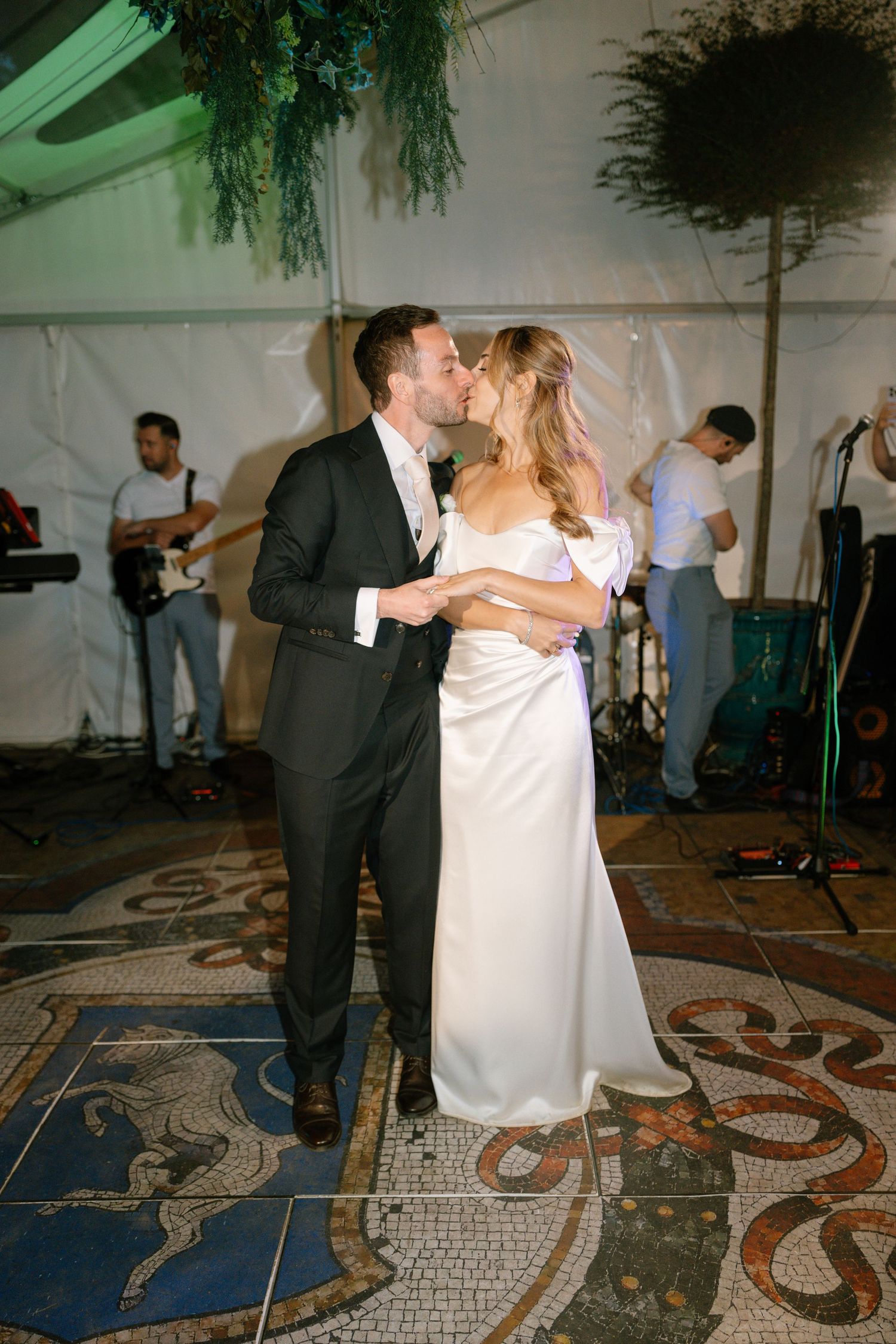 A couple shares a romantic dance moment in front of their wedding band on a decorated dance floor.