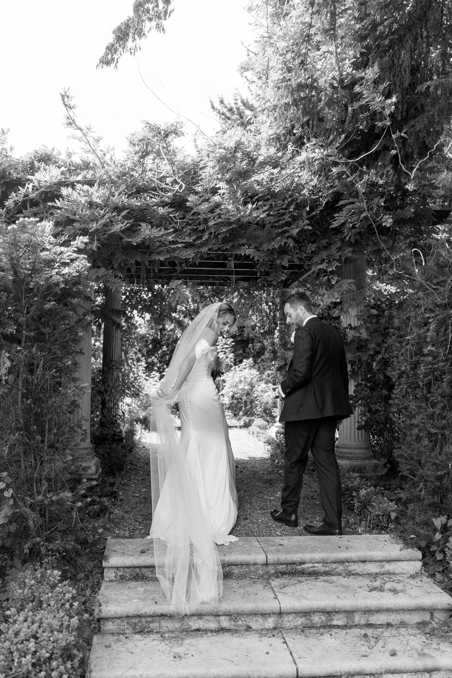 Black and white wedding photos showing couple walking through garden path with lush greenery.