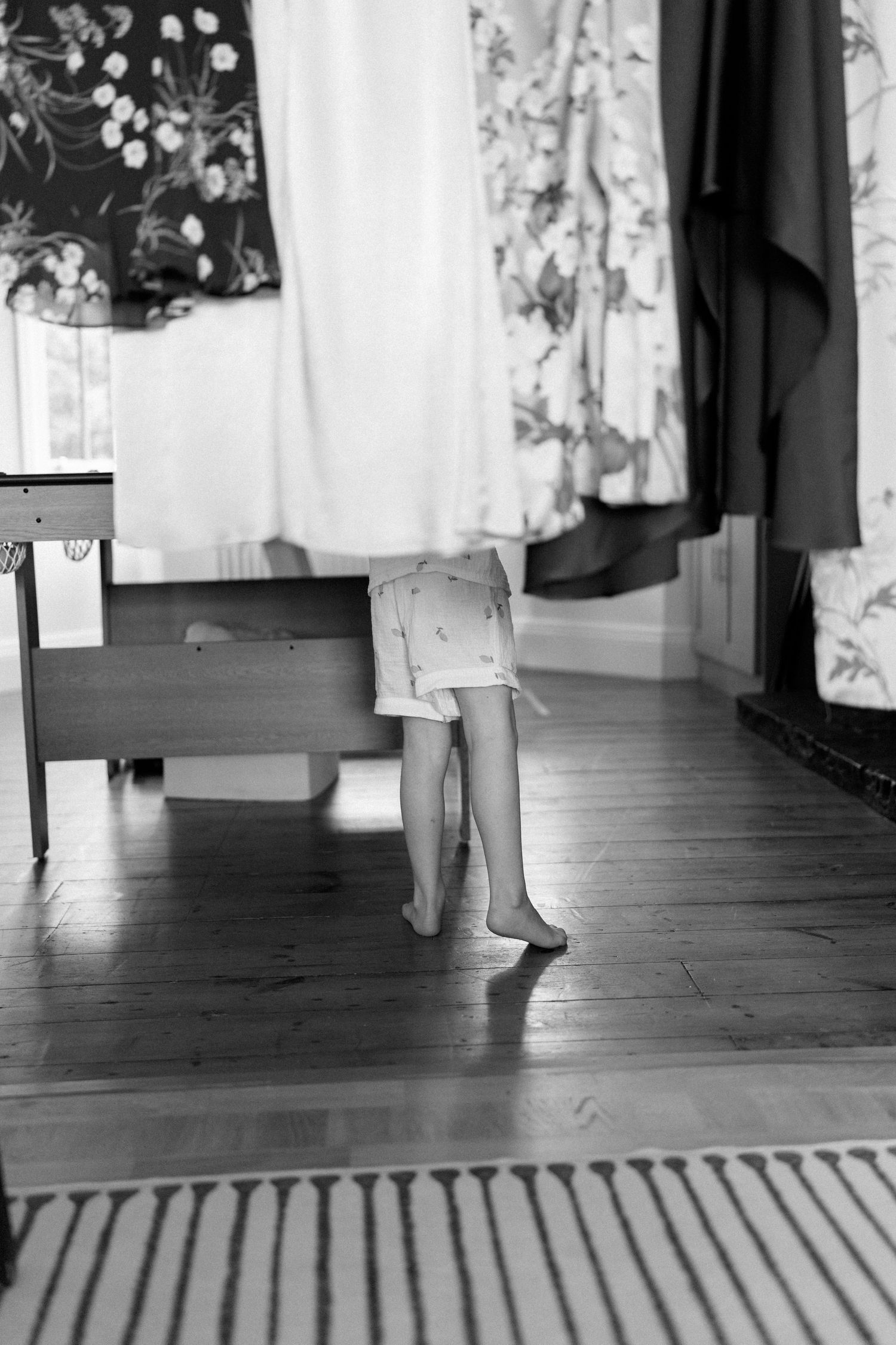 Black and white photo of bare feet on wooden floor beneath hanging clothes.