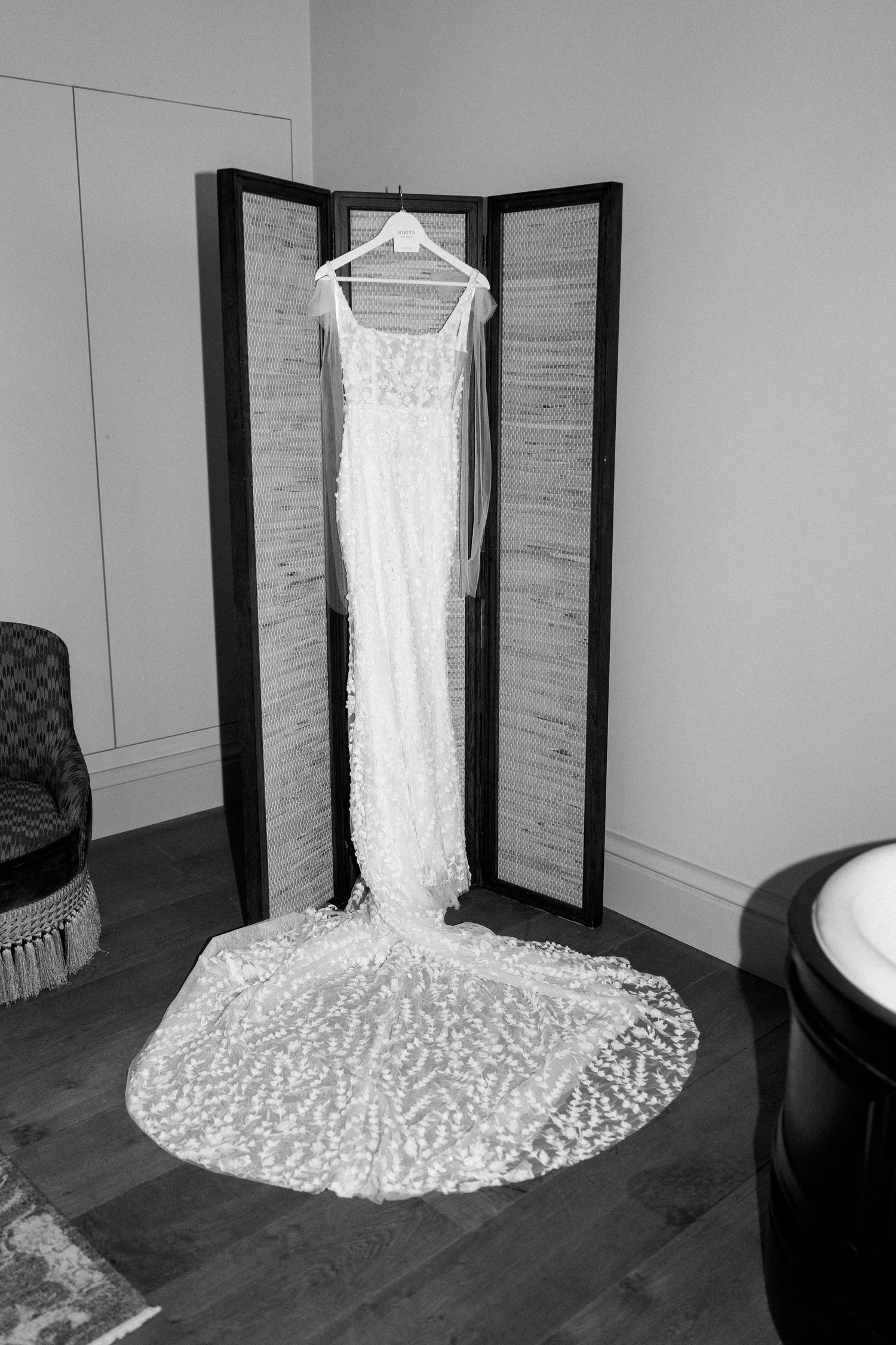 Wedding dress displayed on hanger against folding screen with long lace train flowing.