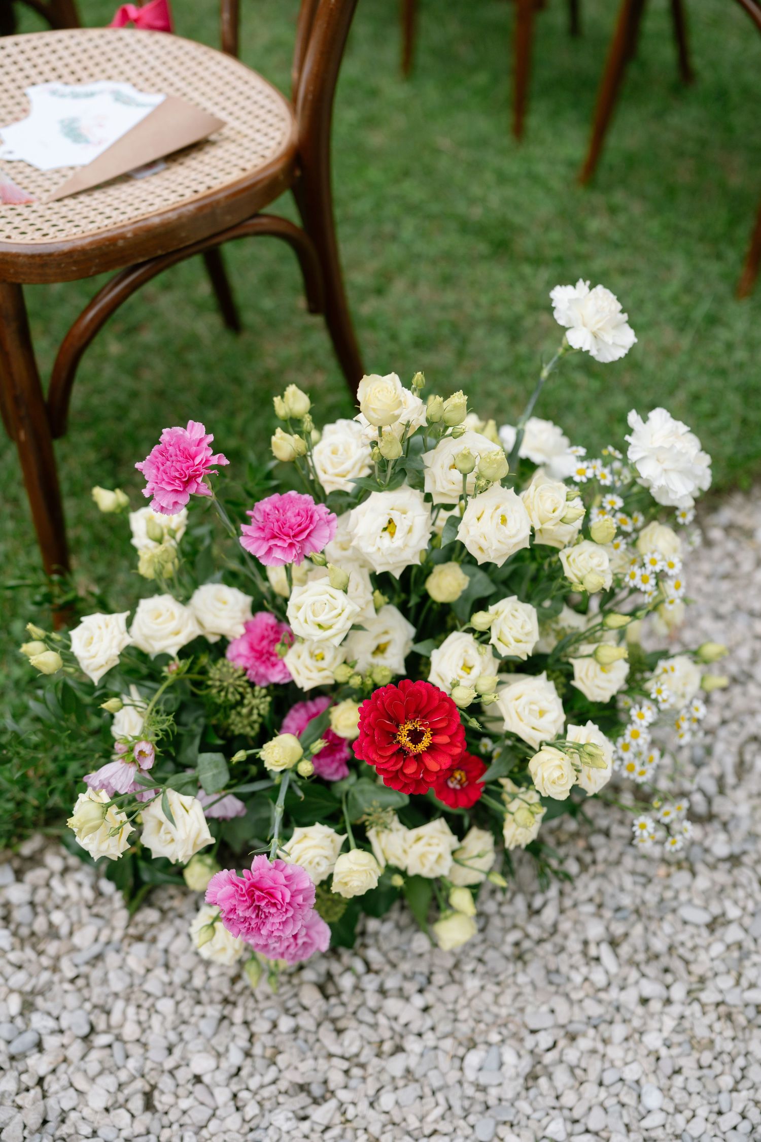 Pink and white flowers line a gravel pathway next to vintage wooden chairs.