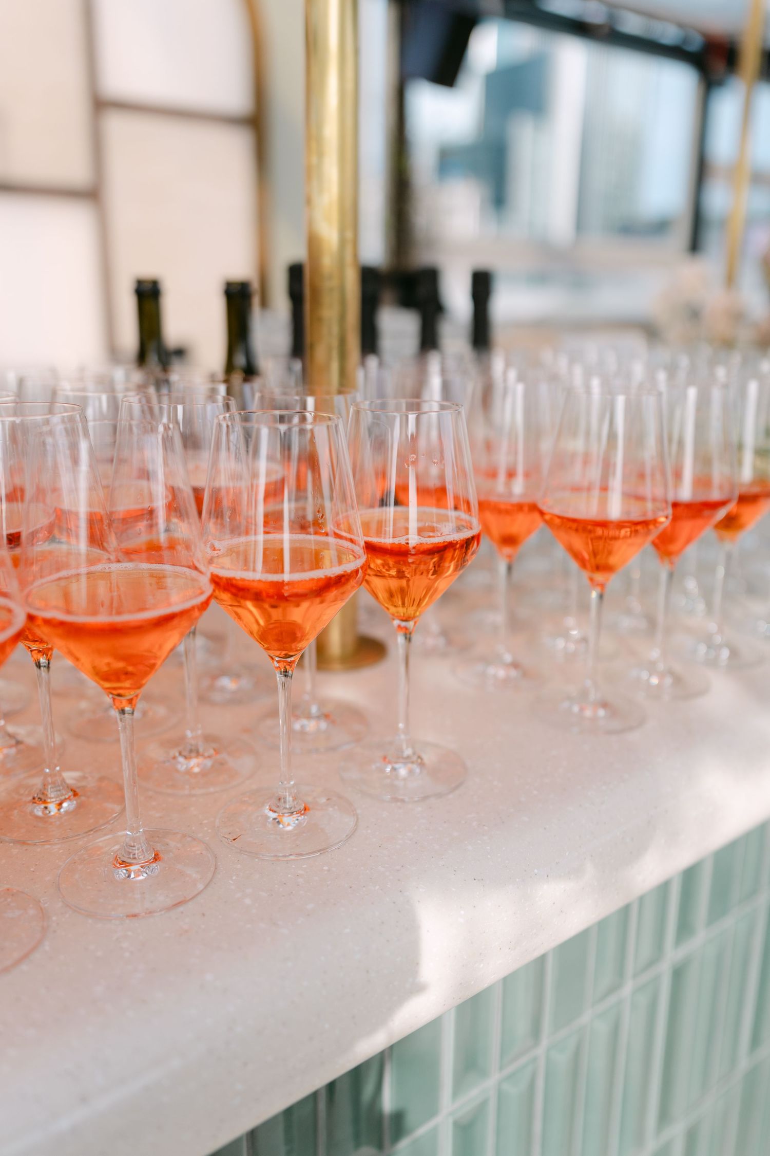 Row of filled champagne glasses with coral-colored cocktails on white counter.