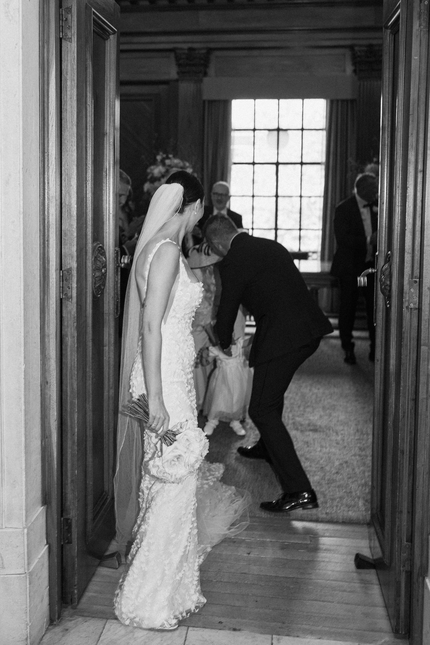 Wedding couple walking through an elegant hallway with wood paneling and tall windows.