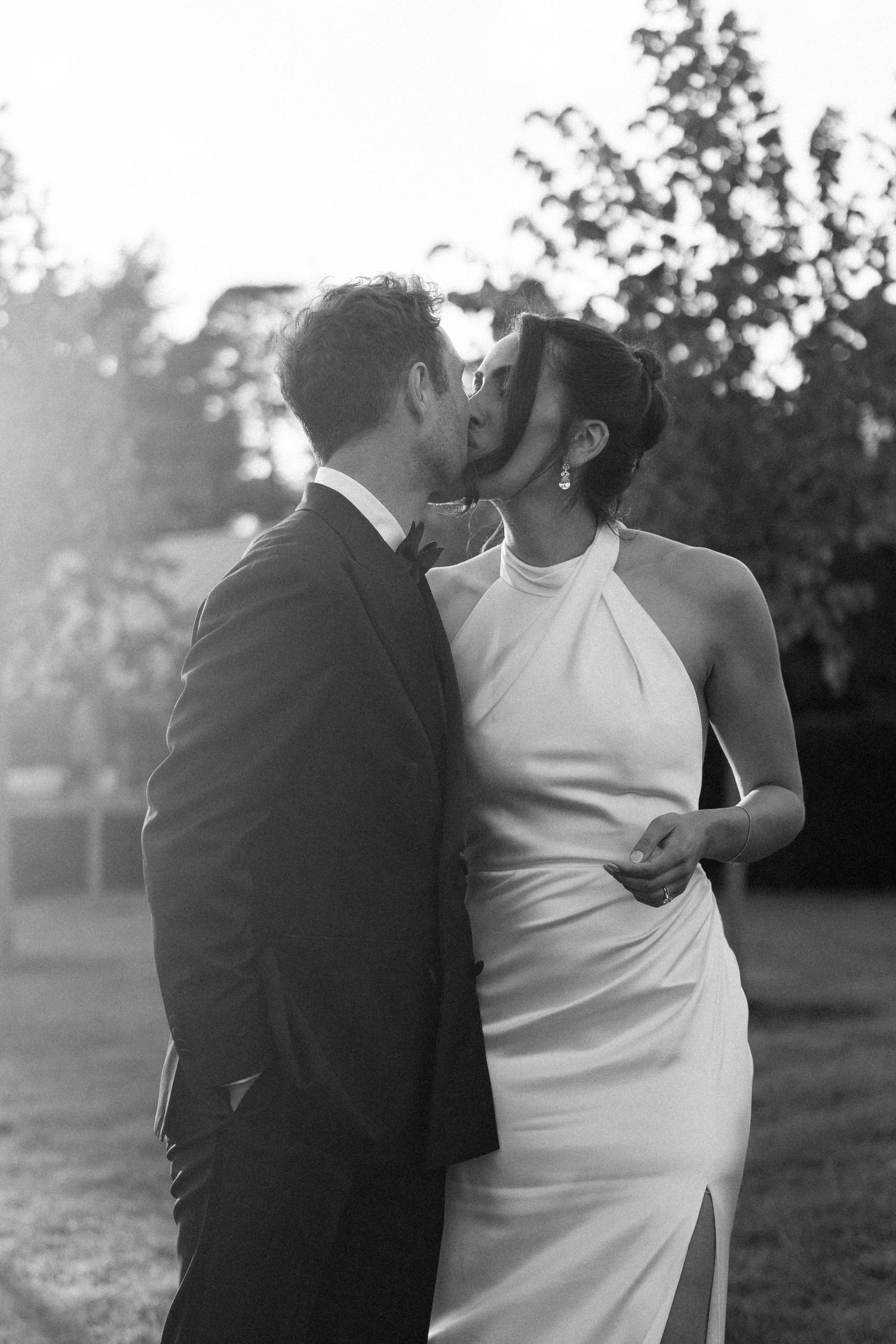 Bride and groom share tender outdoor kiss at golden hour after wedding ceremony.