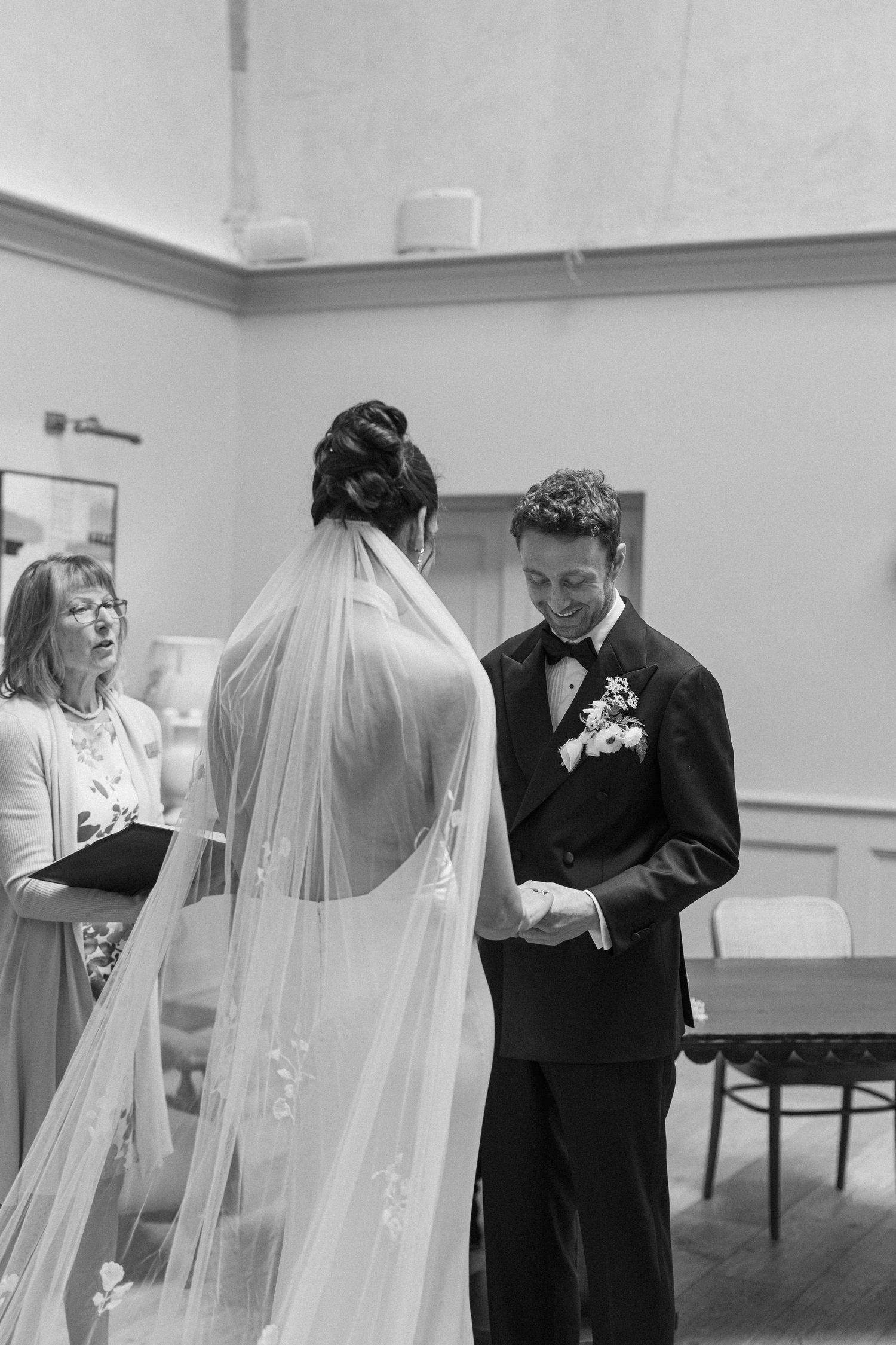 Black and white photo of groom smiling warmly at bride during intimate wedding ceremony vows with officiant.