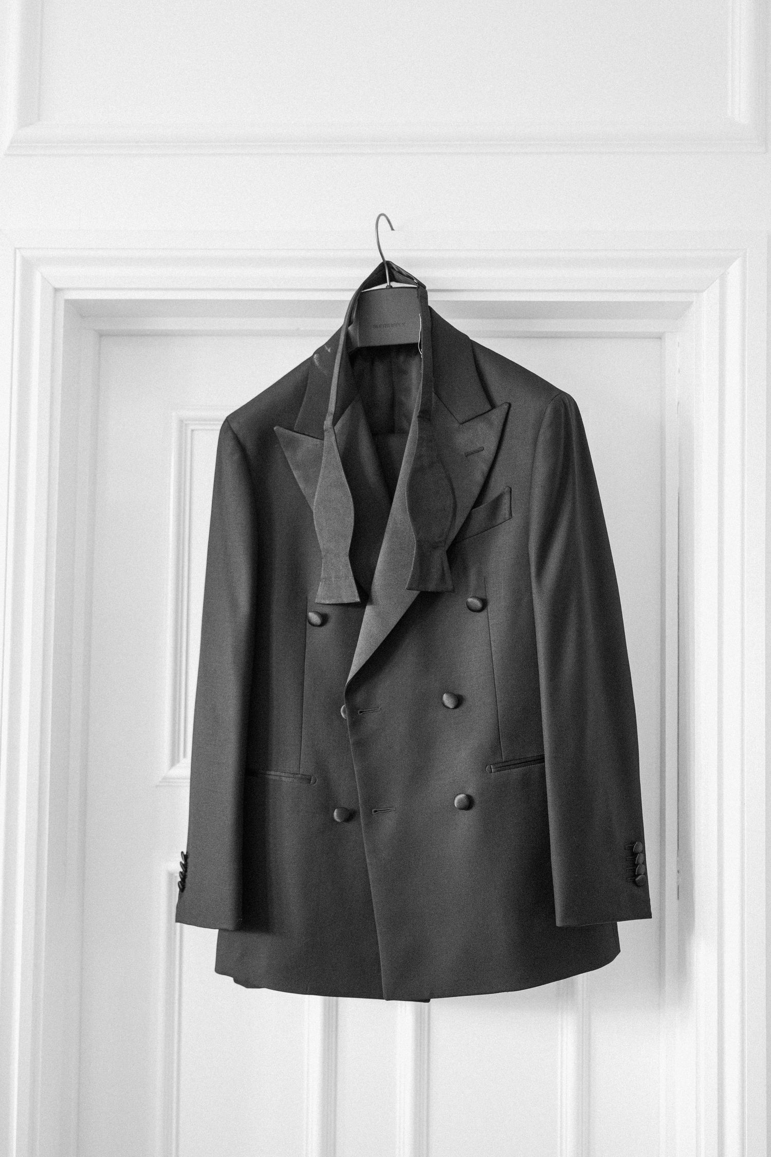 Black and white photo of a double-breasted tuxedo jacket hanging on a white paneled door.