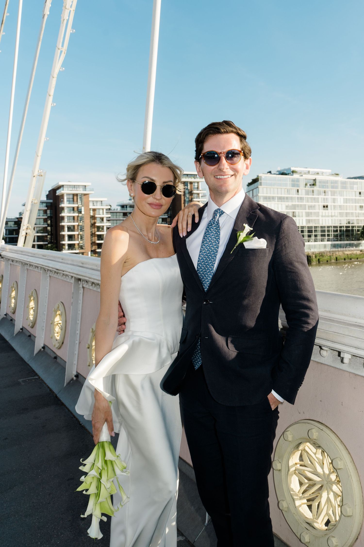 Bride and groom in sunglasses posing on a bridge on their wedding day in London.