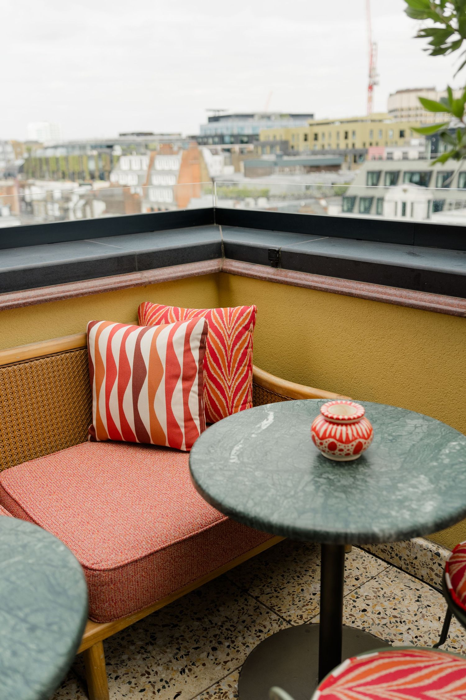Cozy rooftop terrace seating with colorful cushions, marble table, and city skyline views.