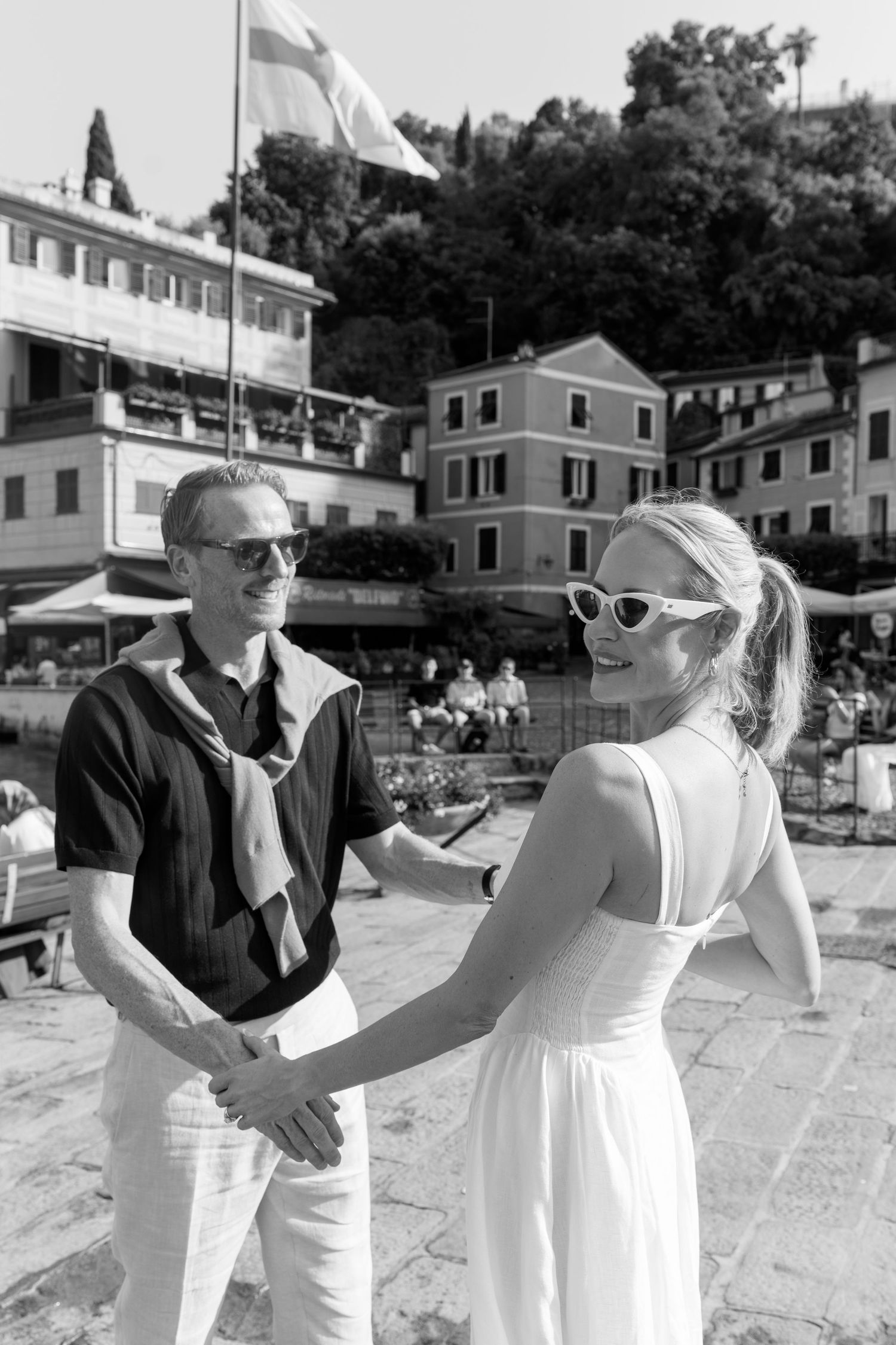 Black and white photo of couple holding hands near Portofino harbor with colorful buildings behind them.