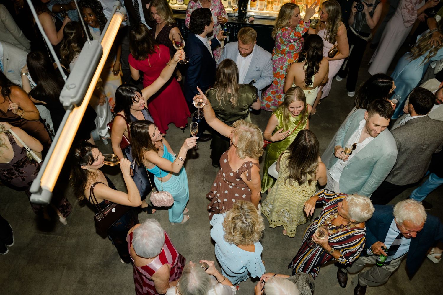 Lively wedding reception dance floor with guests mingling and dancing under warm lights in a modern venue.