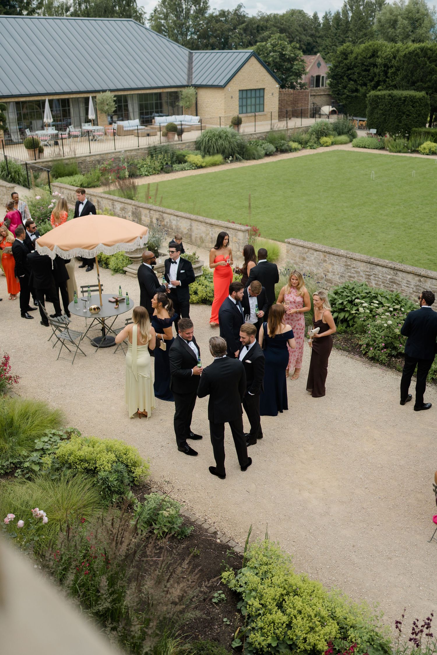 Aerial view of elegantly dressed wedding guests mingling in a formal garden courtyard.