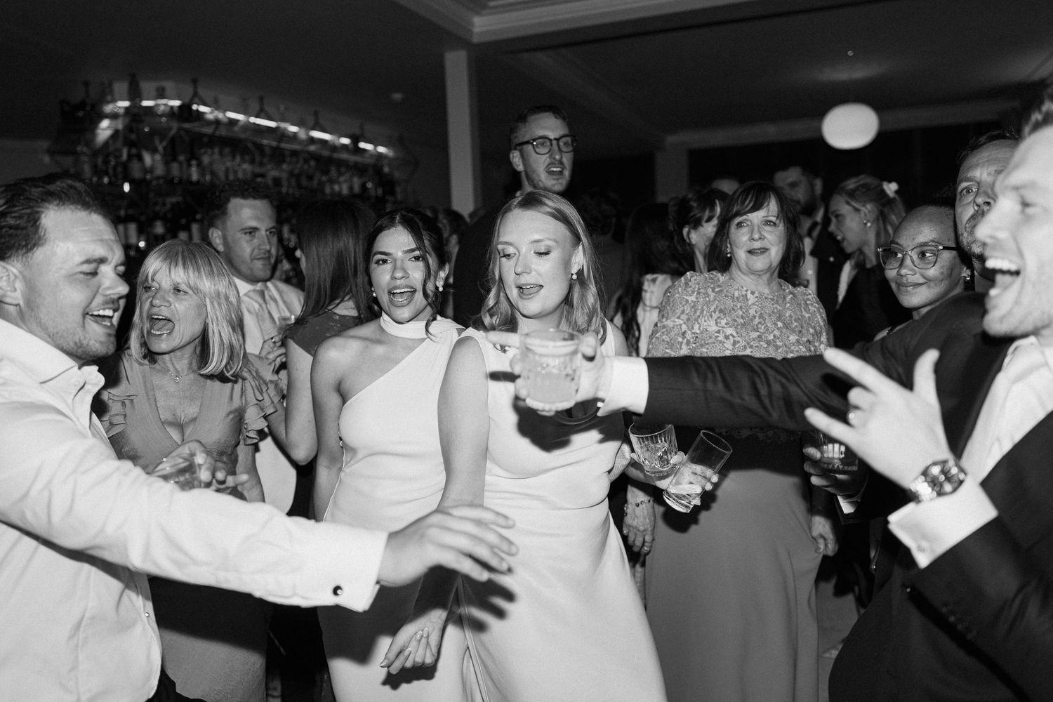 Bride laughing and dancing joyfully with wedding guests at a lively black and white reception.