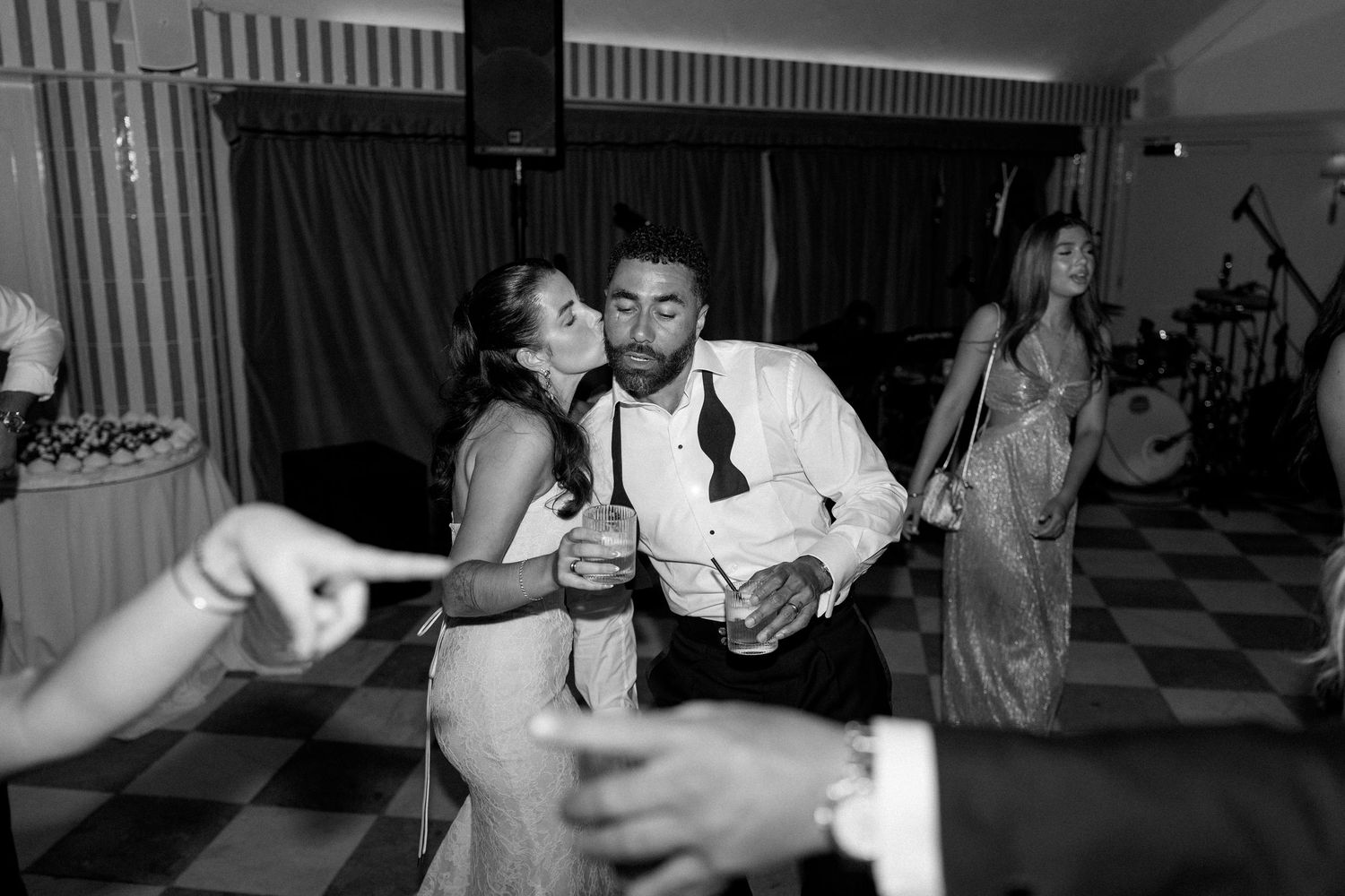 Couple sharing a kiss while dancing at a lively black and white wedding reception party.