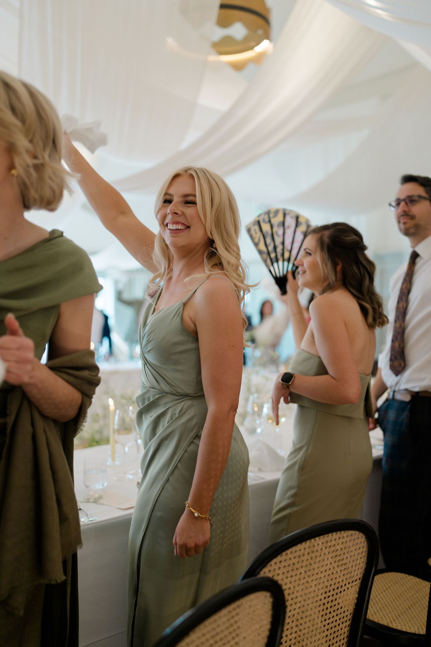 Smiling bridesmaid in sage green dress dancing at elegant wedding reception.
