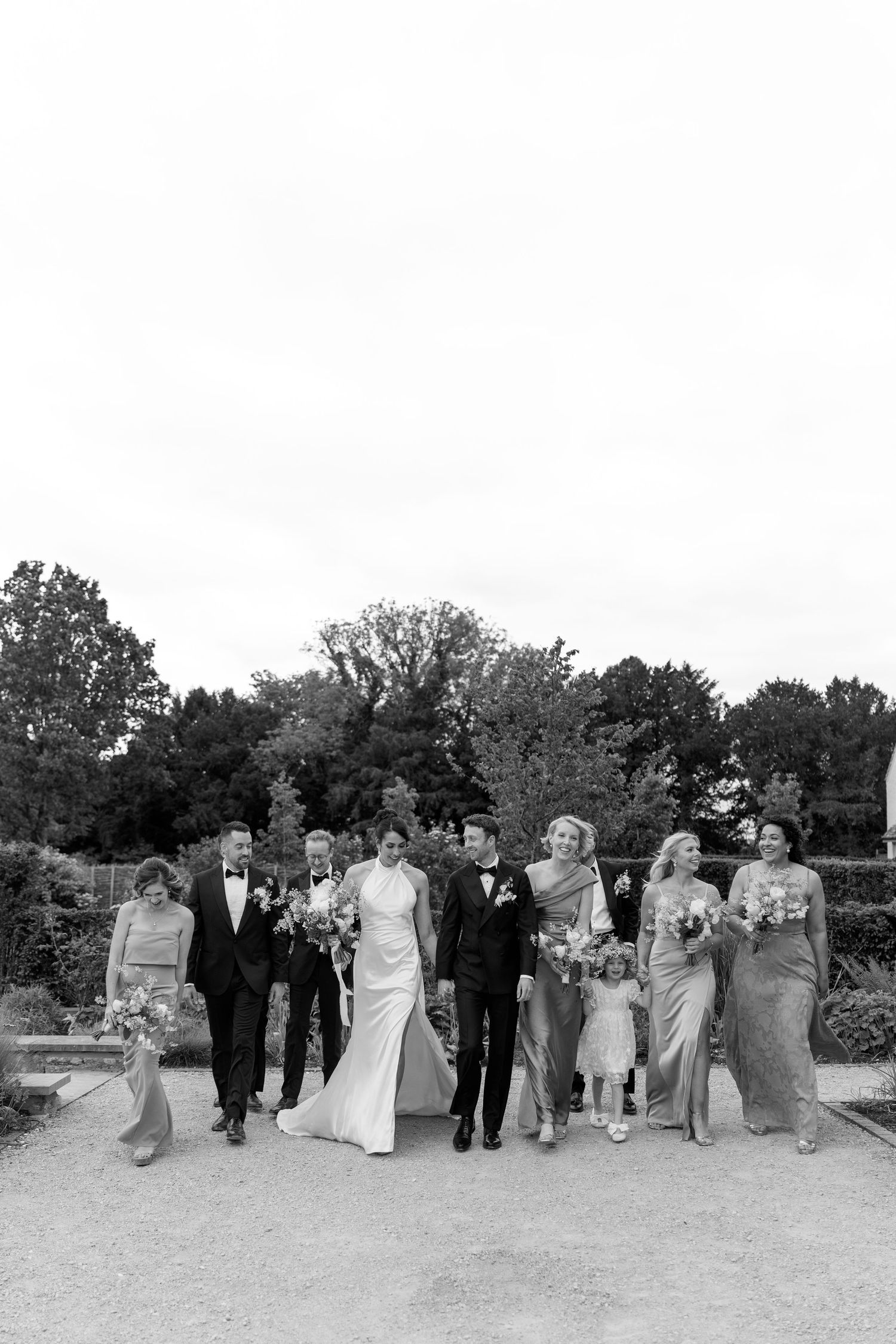 Black and white photo of wedding party walking together outdoors in a garden setting.
