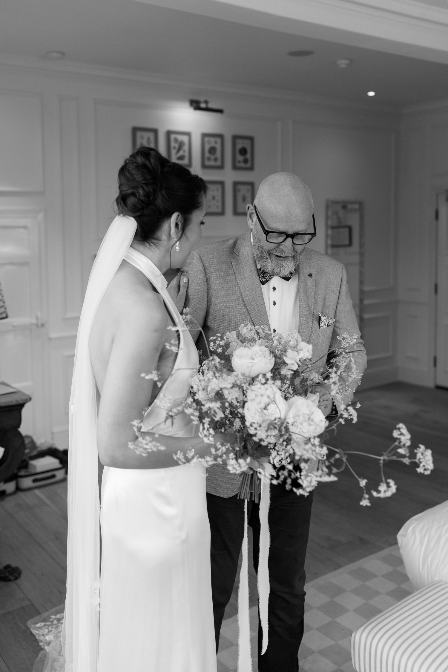Black and white photo of bride receiving floral bouquet from older gentleman in suit before wedding ceremony.