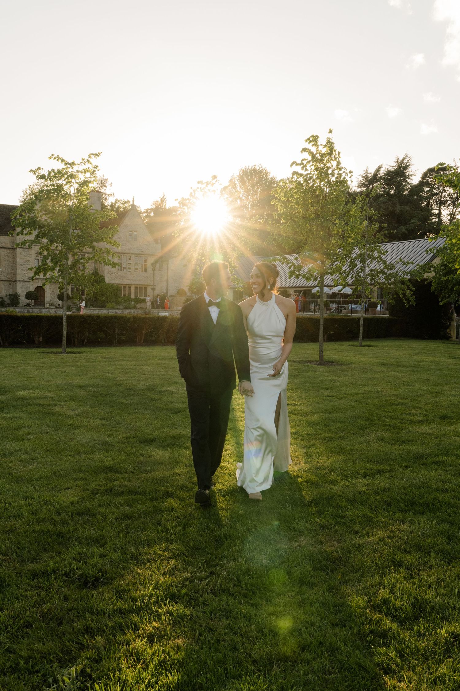 Bride and groom share romantic sunset moment on lush green lawn with golden lens flare.