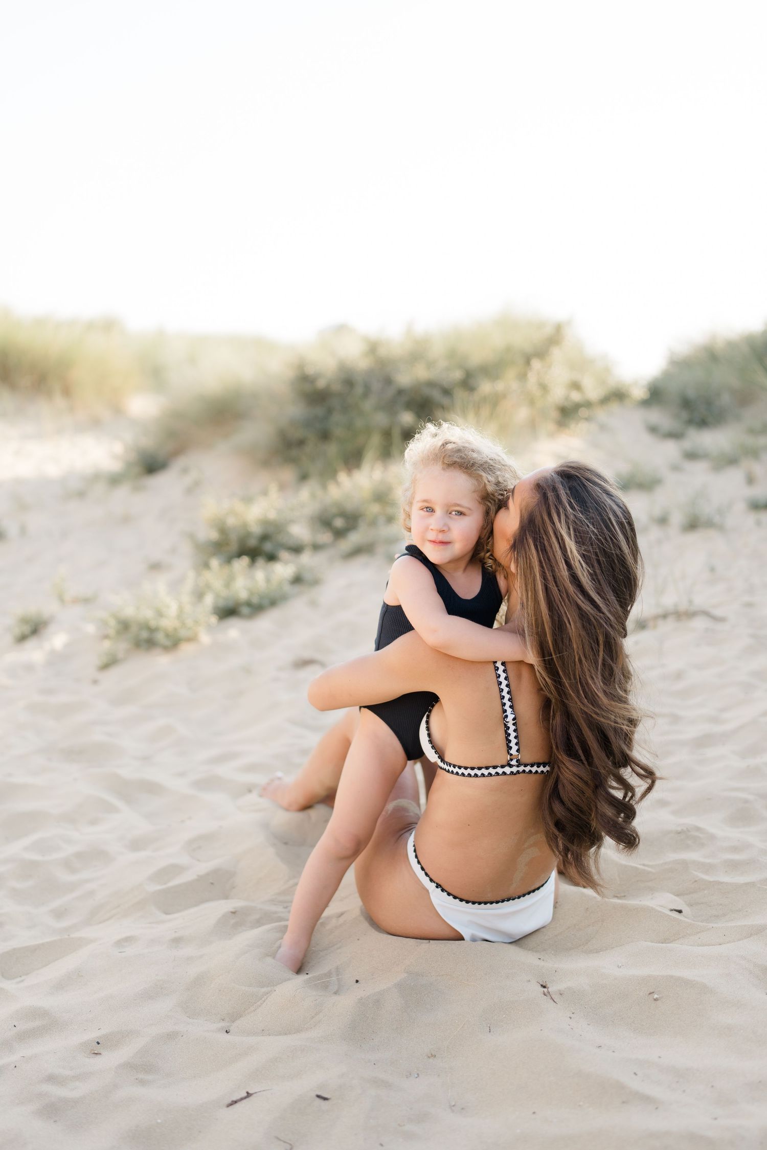 Beachside portrait showing loving embrace between parent and child on sandy dunes.
