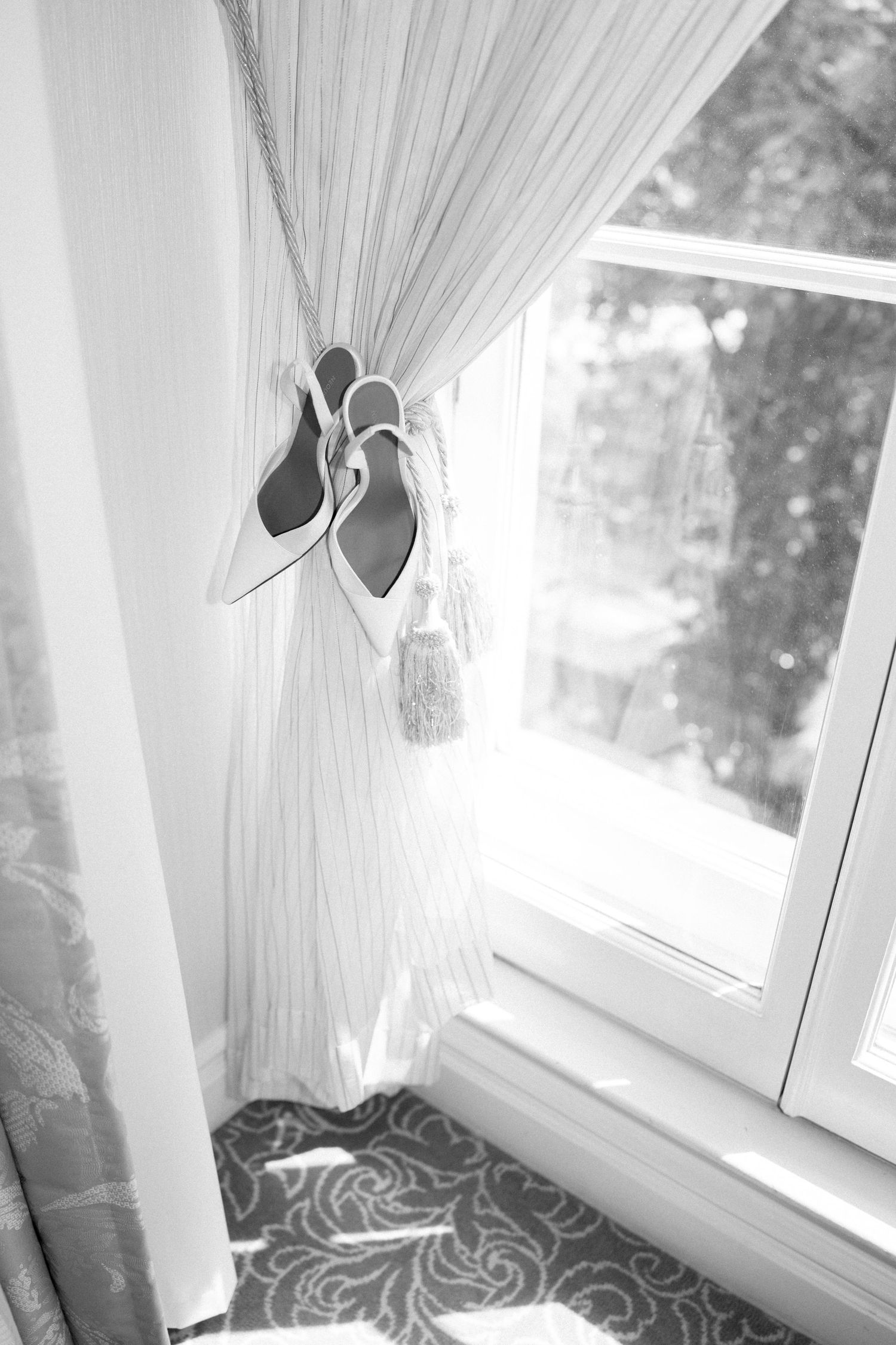 Sunlight streaming through white curtains by a window with shoes on the windowsill.