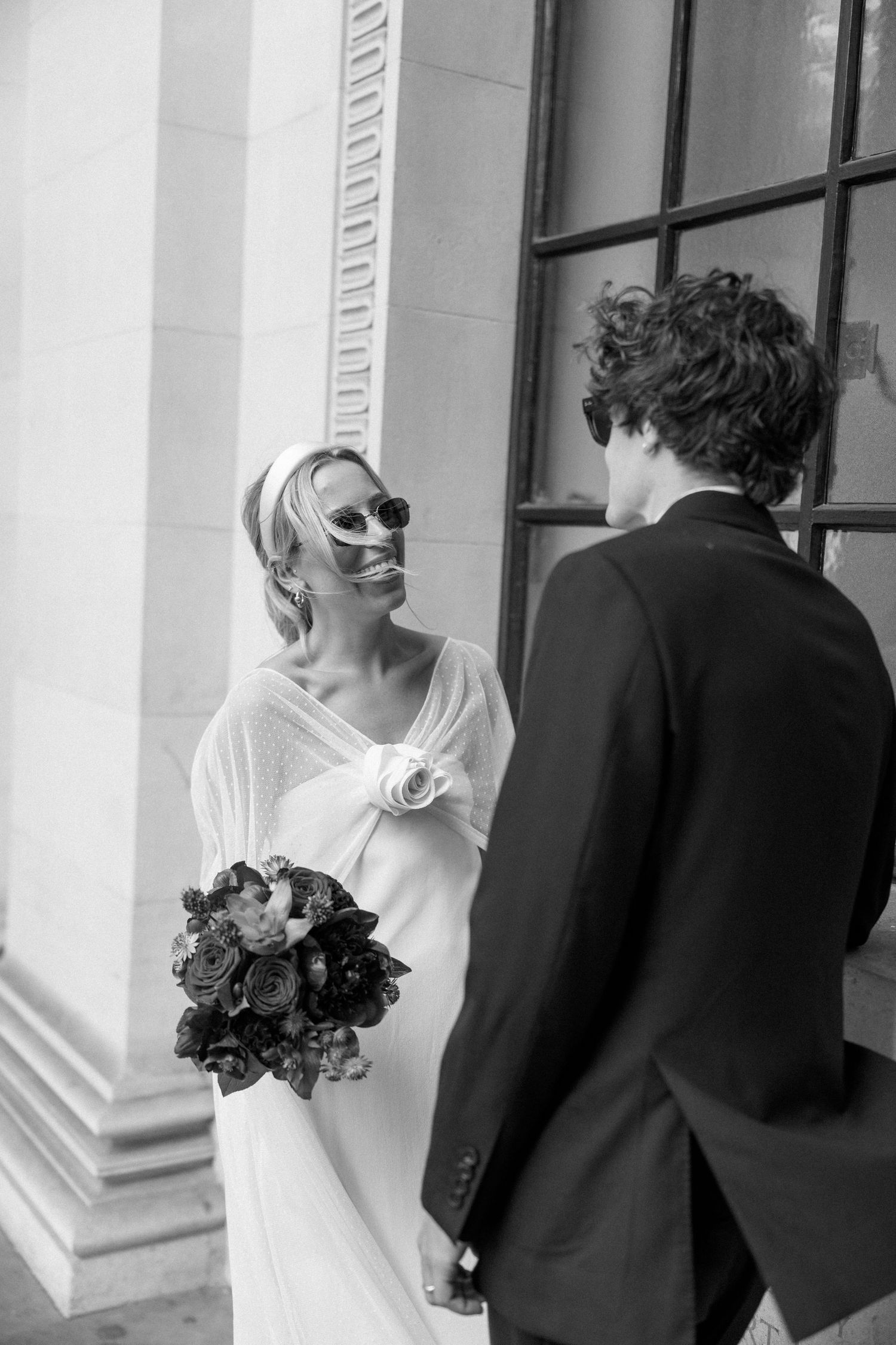 A candid wedding moment captured between classical columns with natural lighting.