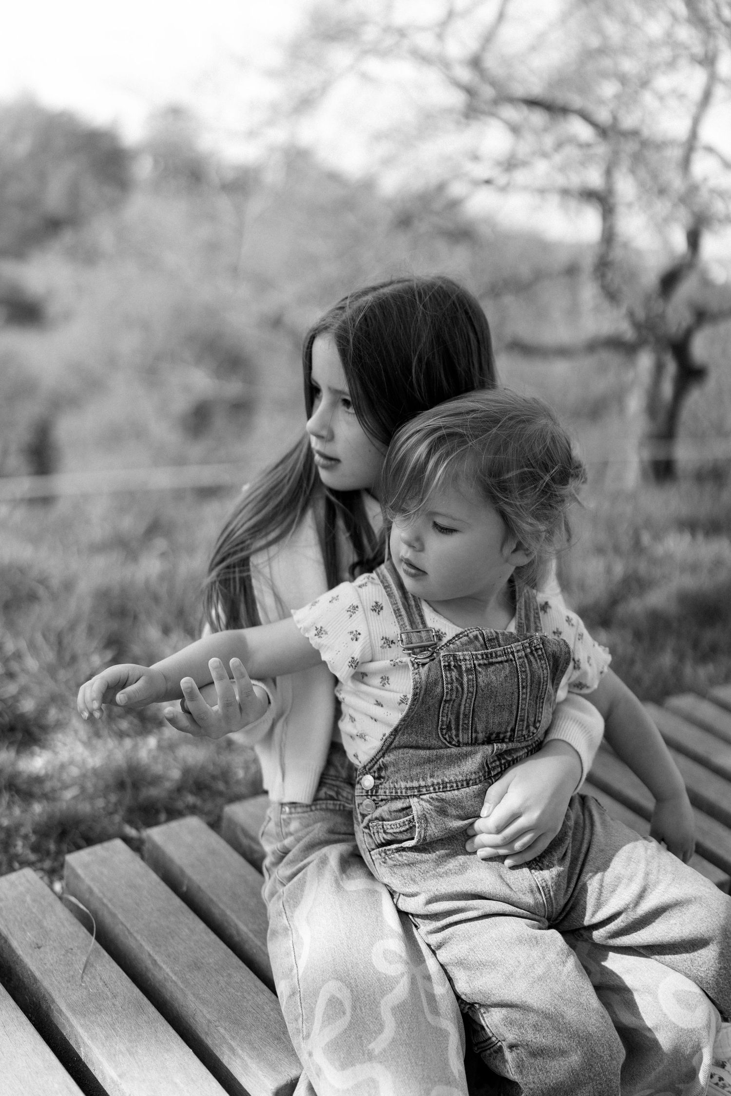 Two figures sit together on a wooden bench in a black and white photograph.