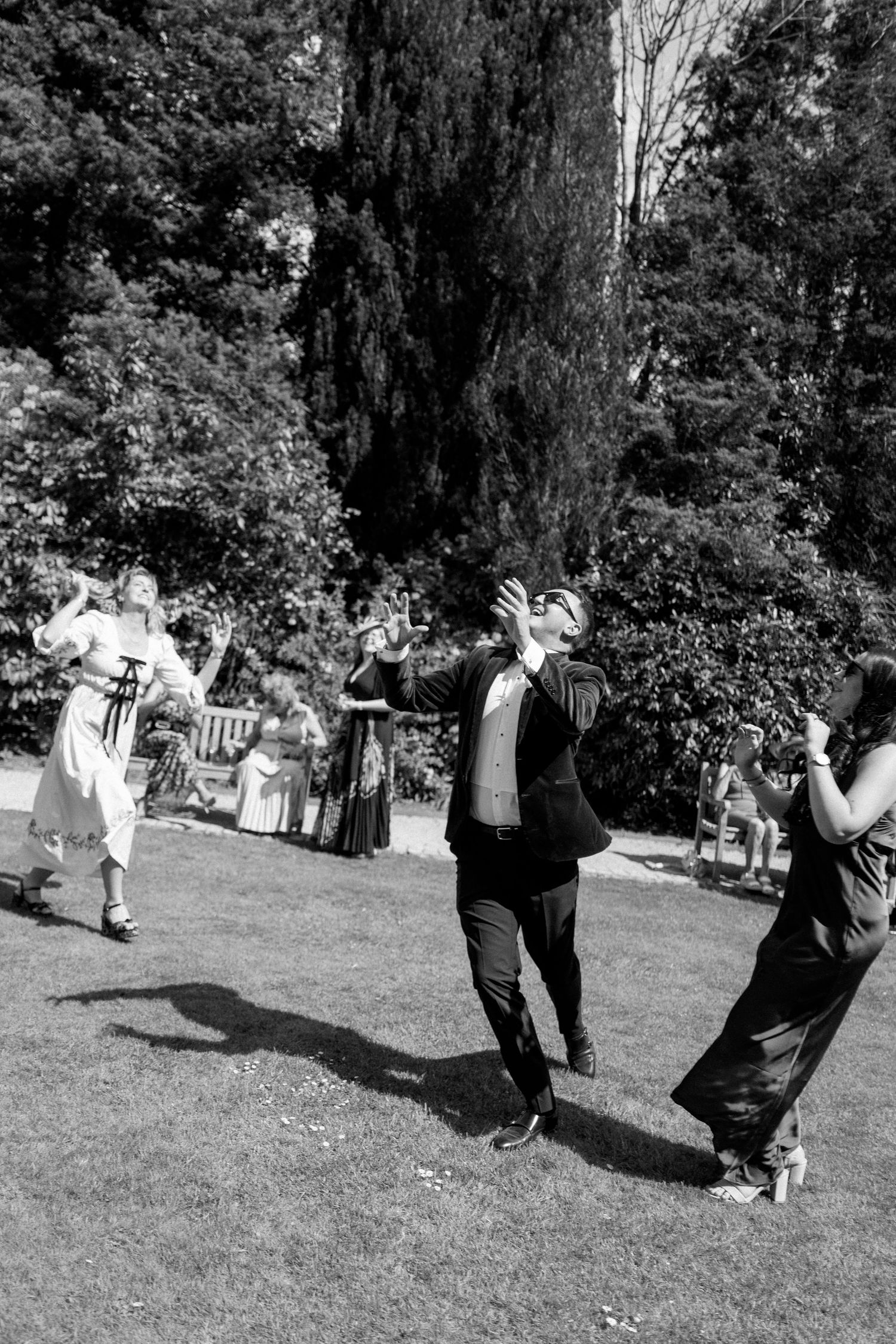 Wedding guests dance joyfully on a lawn during an outdoor celebration.