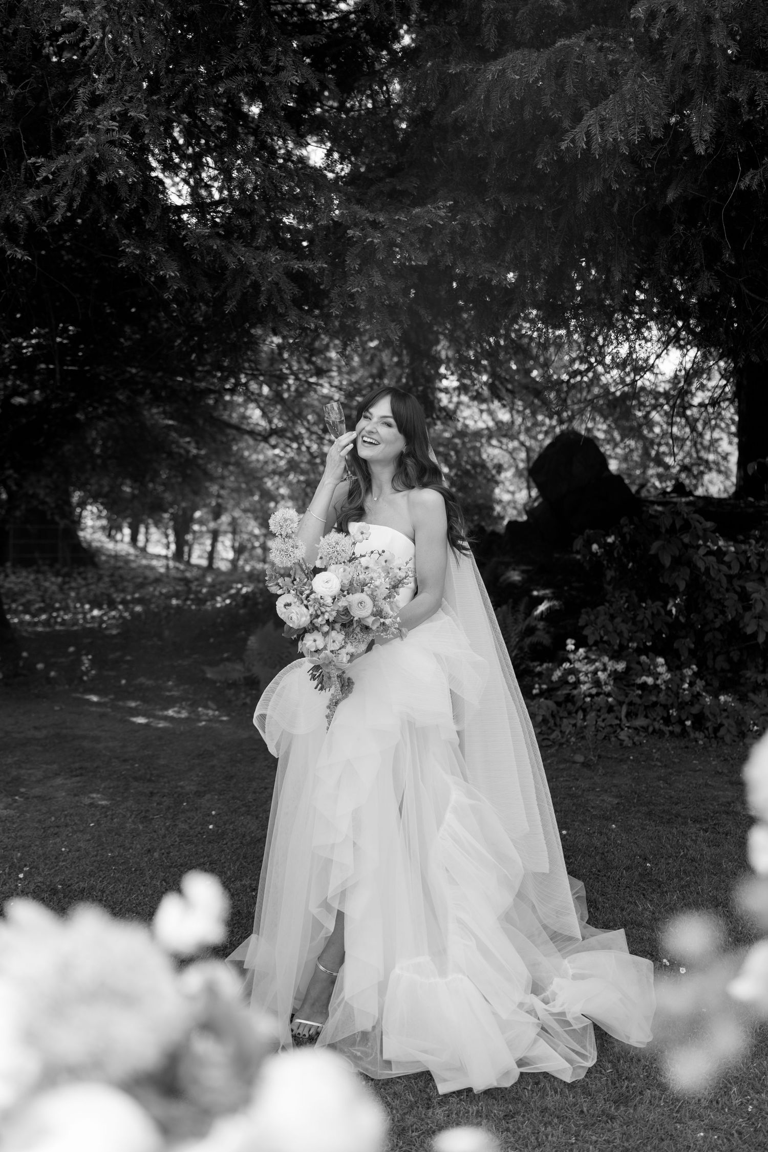 Dreamy black and white wedding photo with flowing dresses in garden setting.