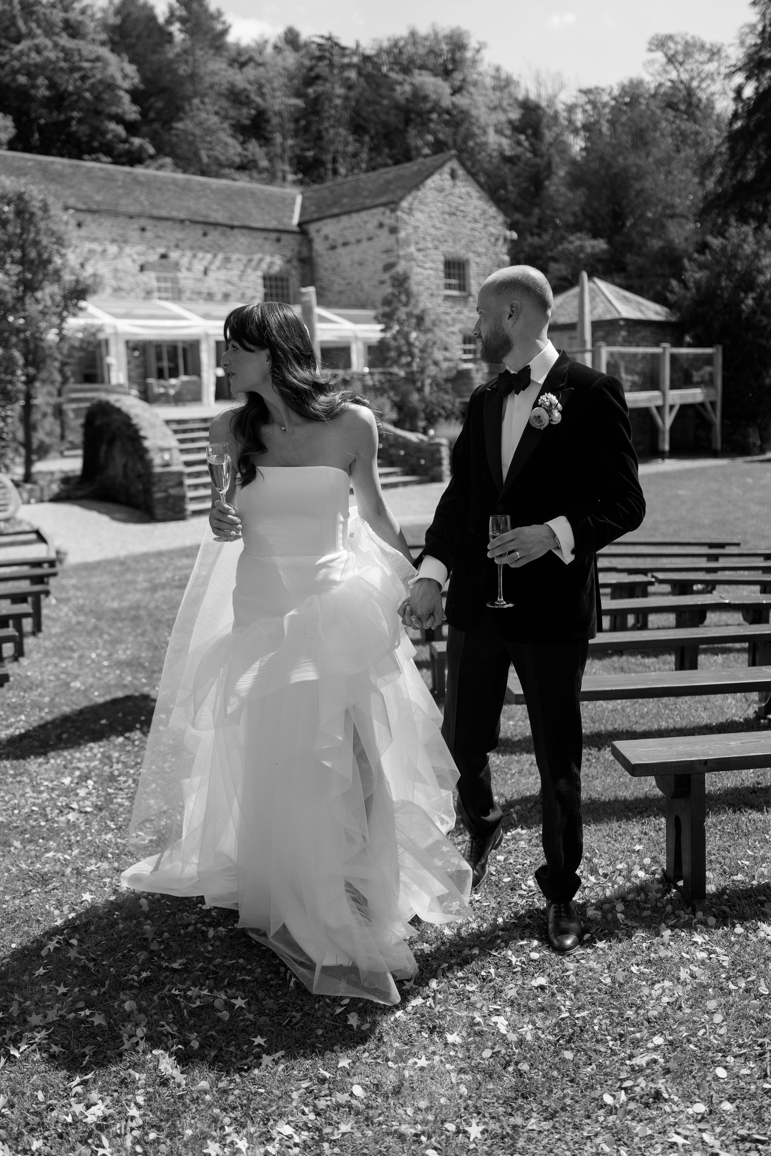 Wedding couple celebrating among scattered petals in front of a historic stone building.