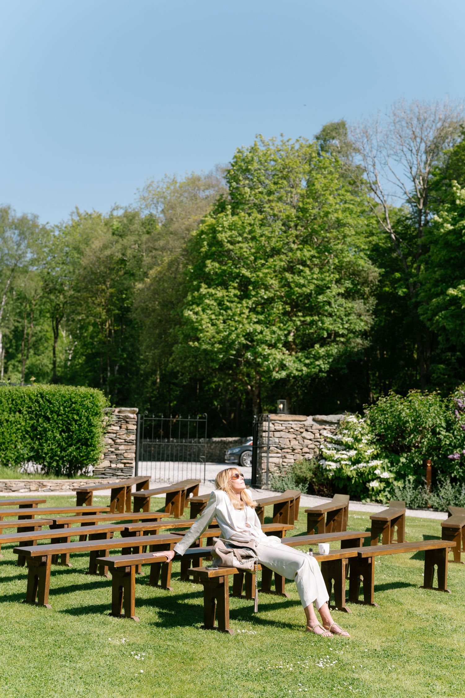 Wooden benches arranged outdoors for a garden ceremony on a sunny day.