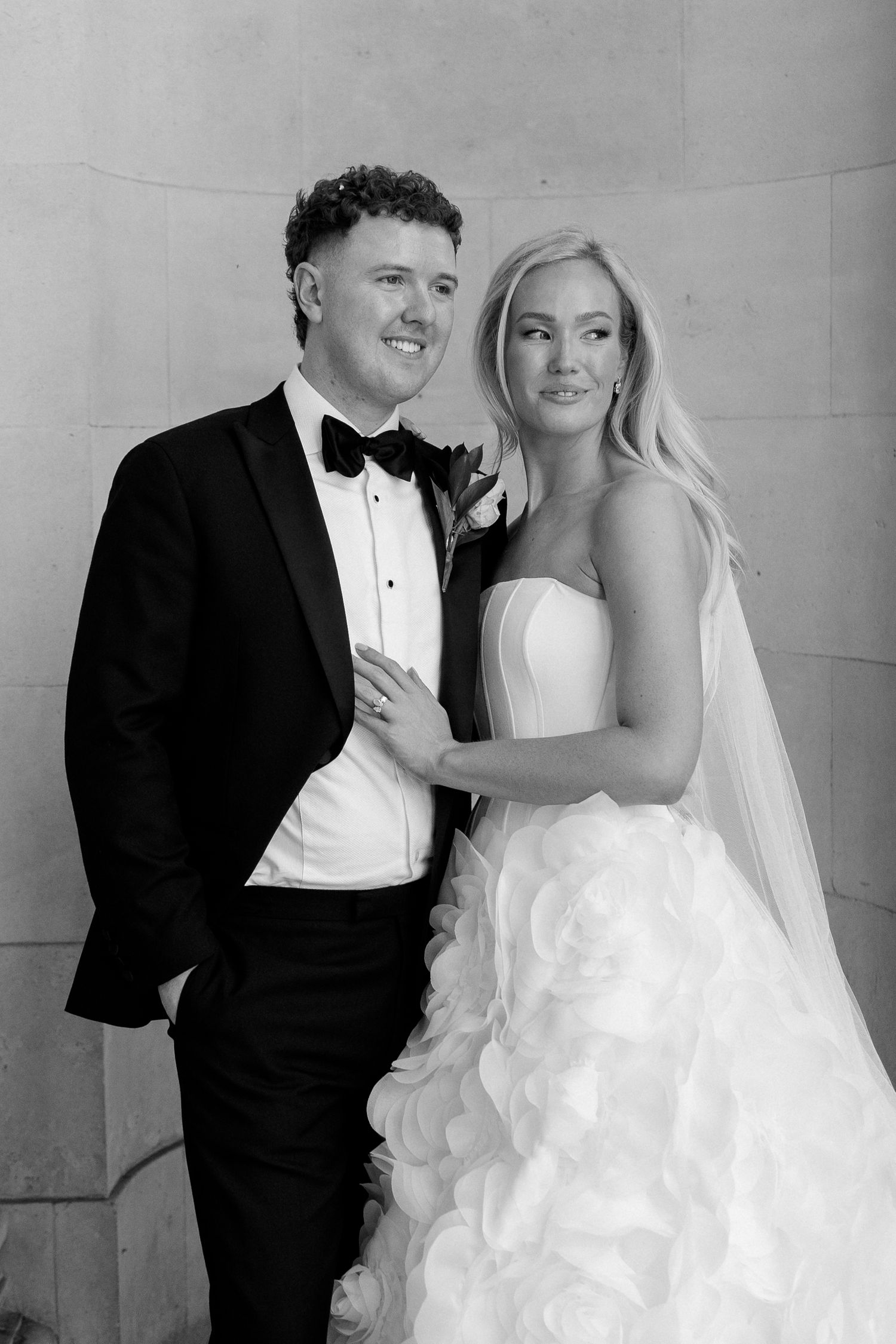 Black and white wedding portrait of a smiling groom in tuxedo and bride in strapless ruffled gown with veil.
