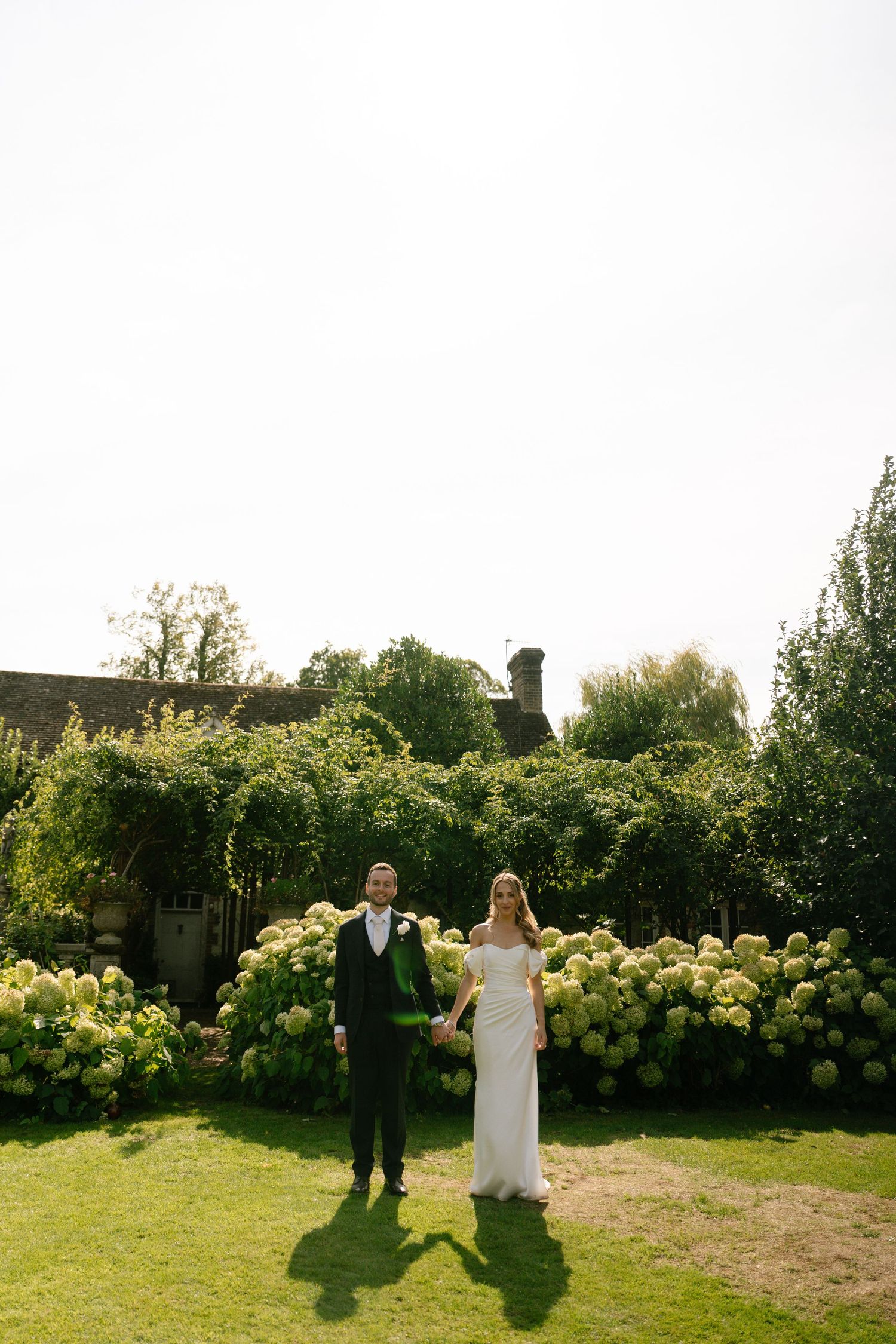 A couple poses against a backdrop of lush hydrangea bushes in a garden setting.